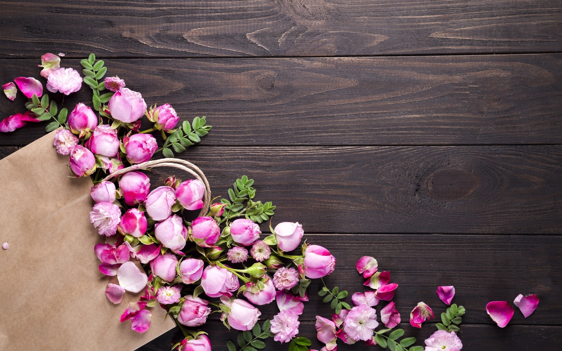 Цветки розовой розы с бумажным пакетом  на деревянном фоне