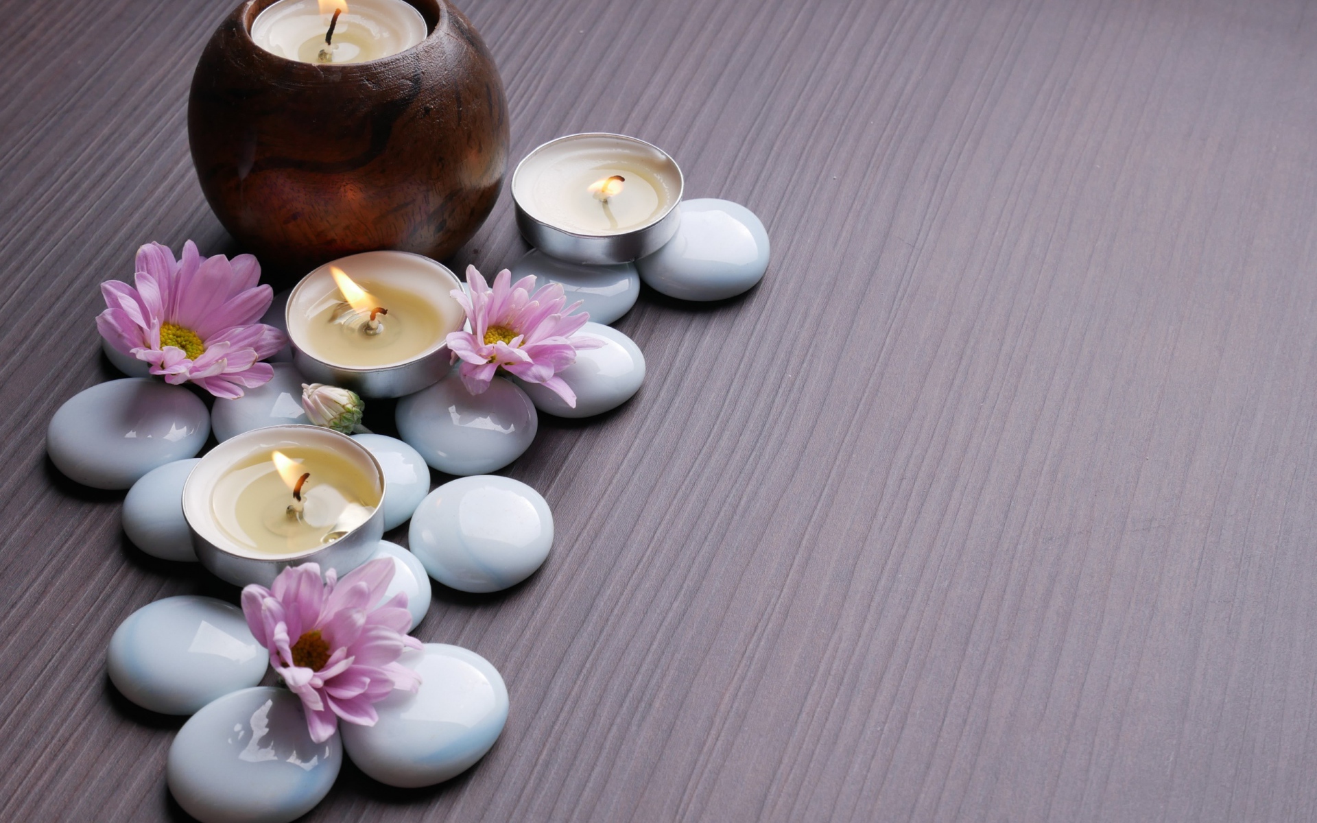 Камни с хризантемами и зажженными свечами на столе 