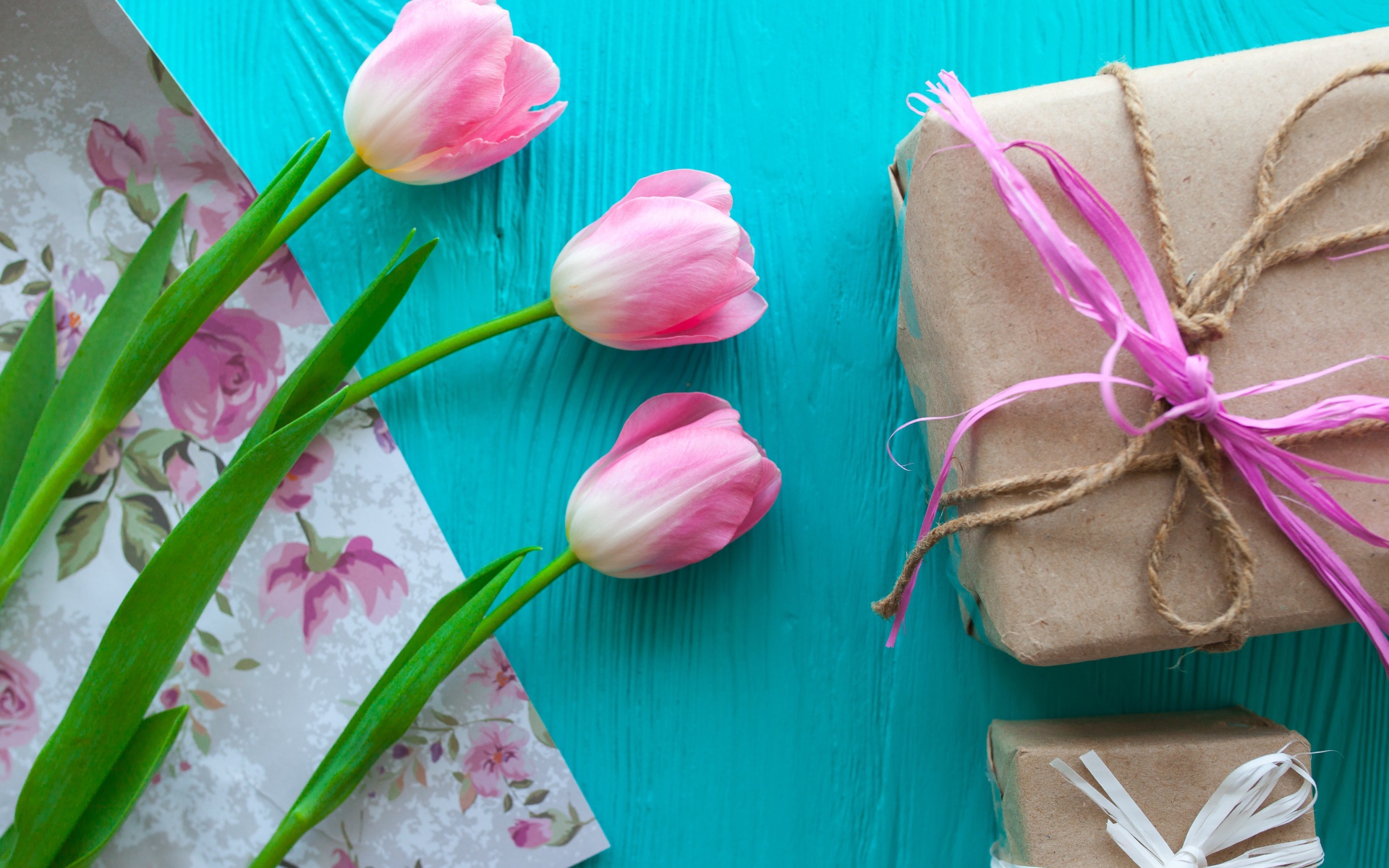 Три розовых тюльпана на голубом столе с подарками