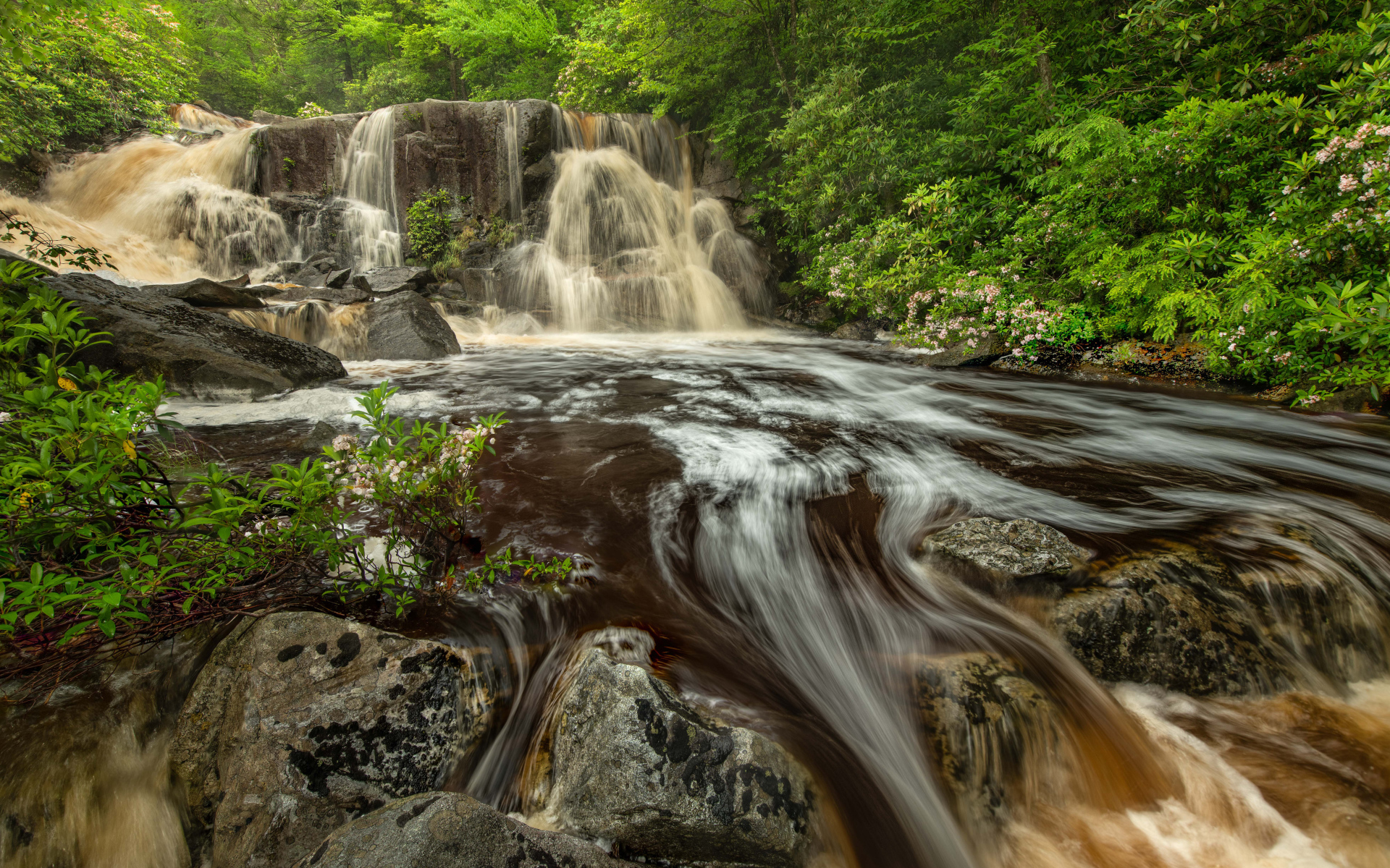Быстрая холодная вода водопада стекает по большим камням