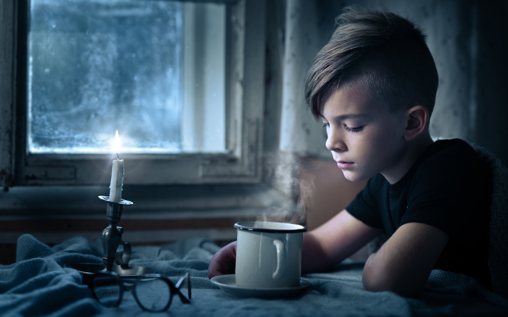 Маленький мальчик сидит за столом при свете свечи 