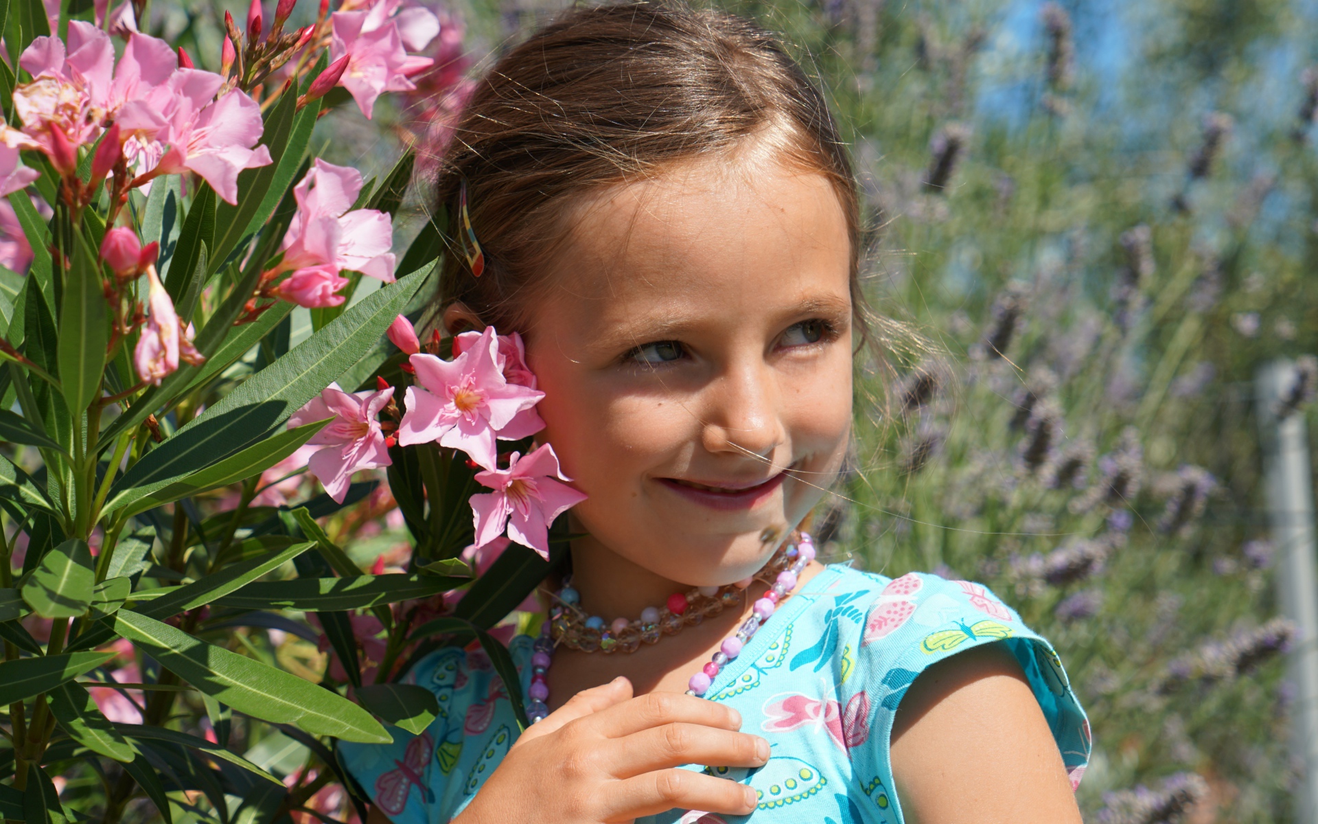 Маленькая девочка стоит у растения с розовыми цветами 