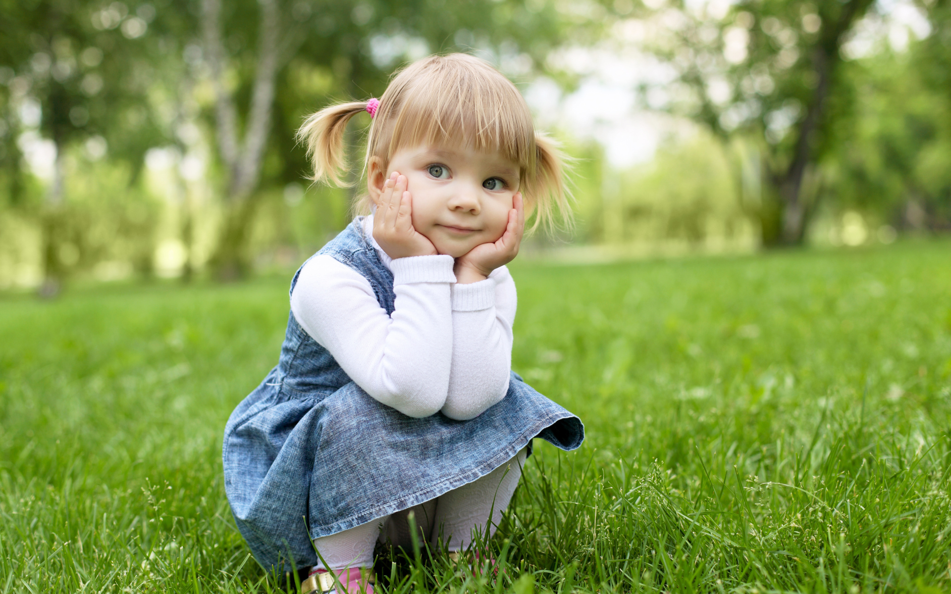 Маленькая девочка в сарафане сидит на траве 