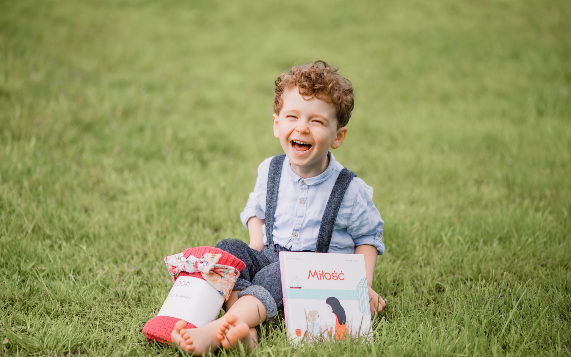 Улыбающийся маленький мальчик сидит на зеленой траве