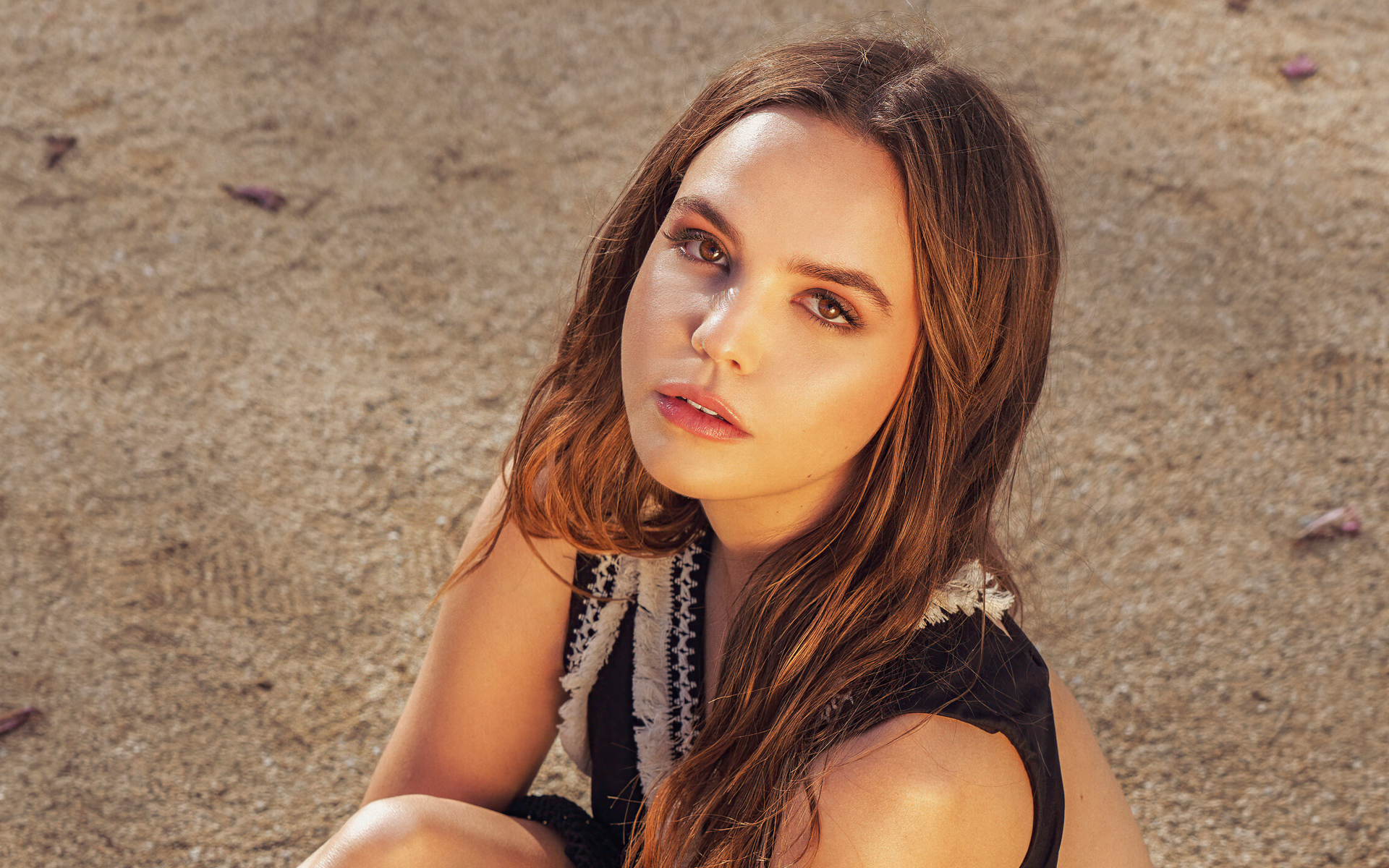 Кареглазая актриса Бэйли Мэдисон сидит на песке