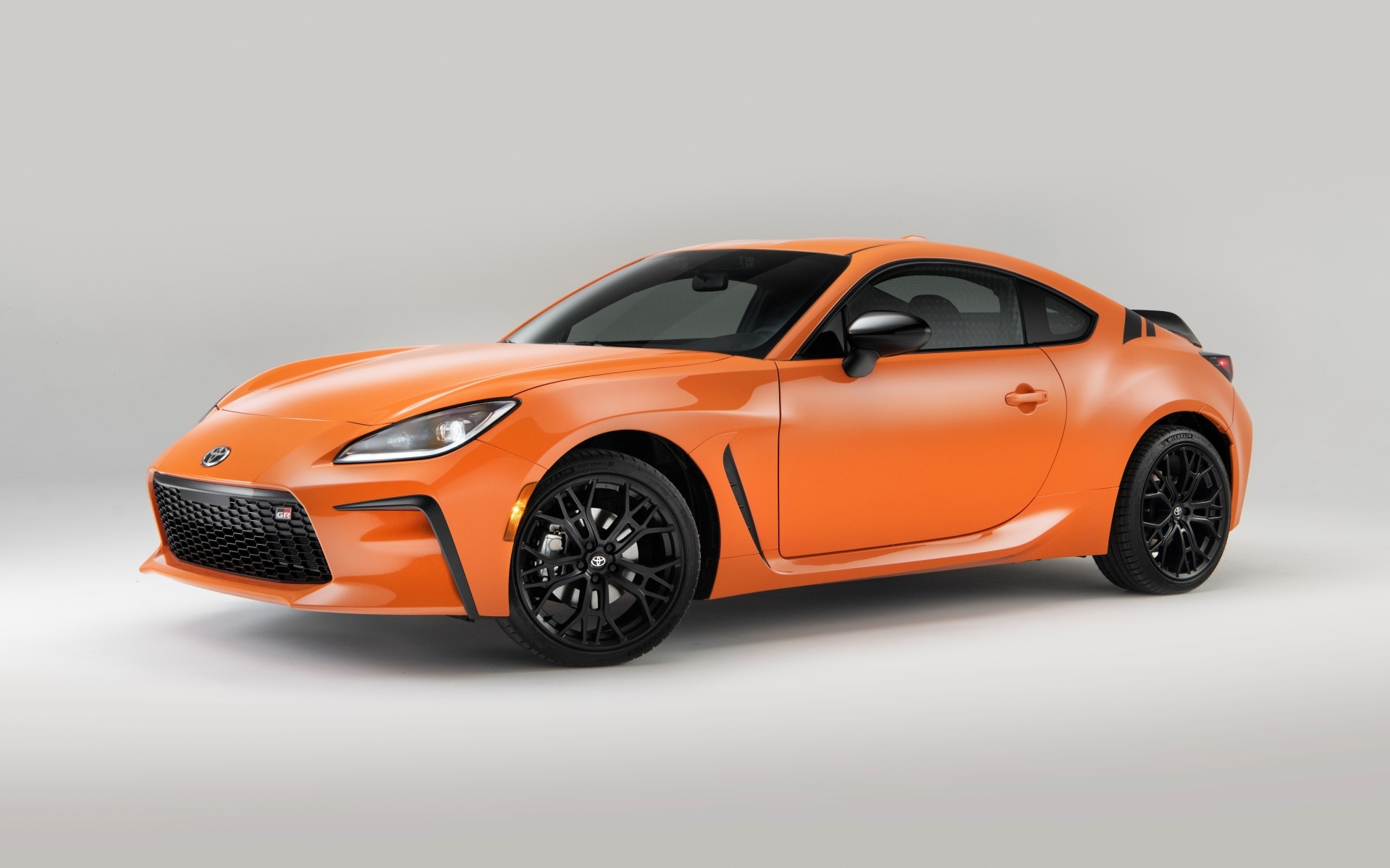Оранжевый автомобиль Toyota GR 86 на сером фоне