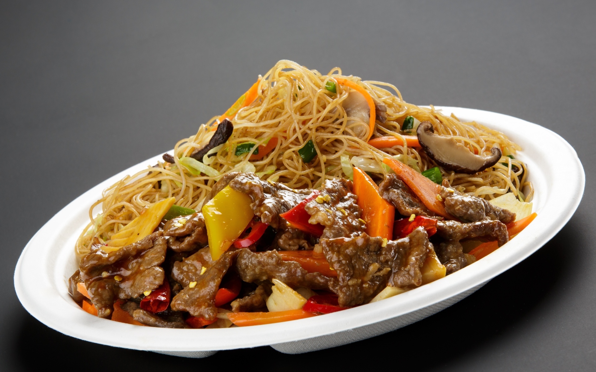 Острая лапша с грибами на белой тарелке на сером фоне