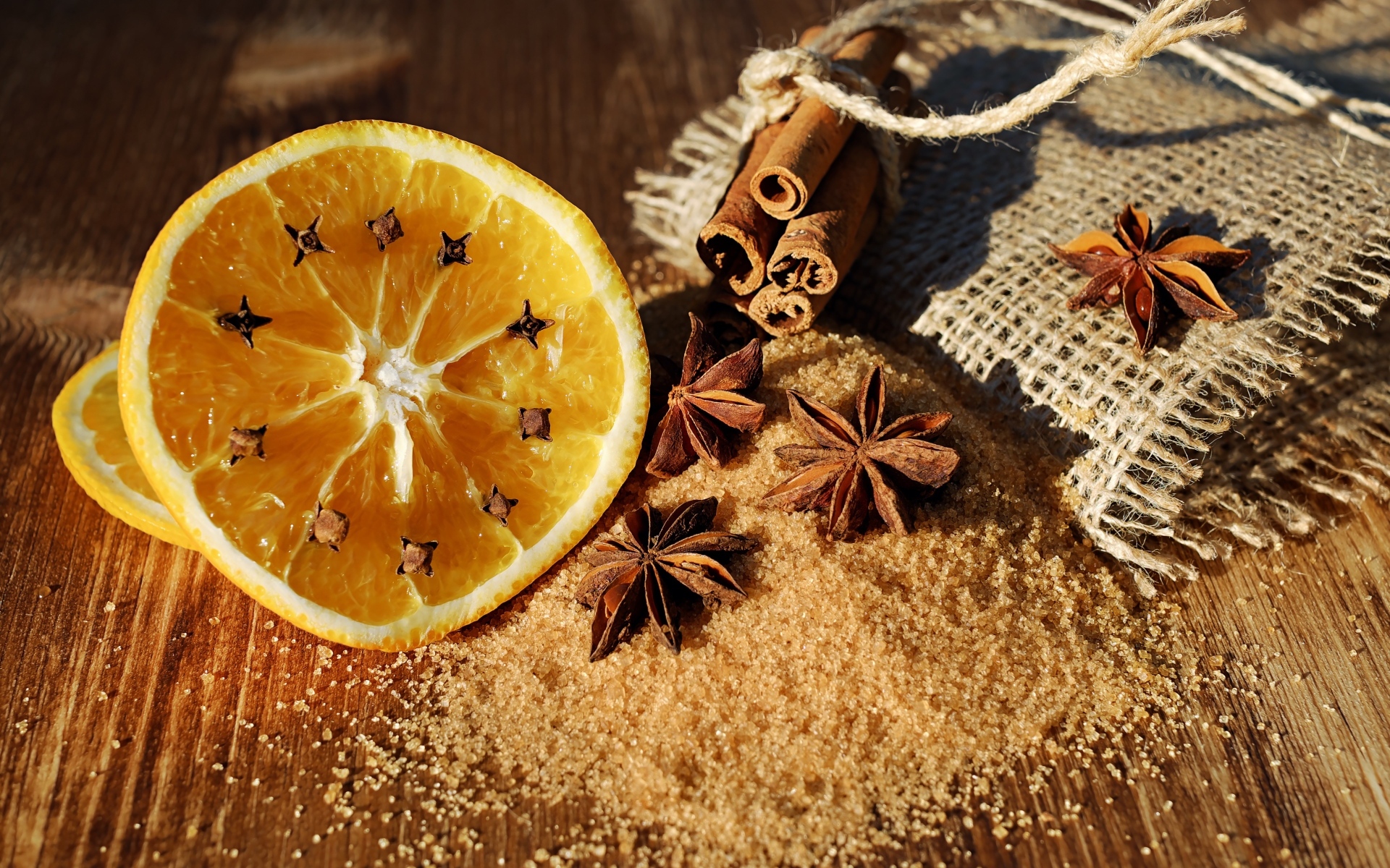 Апельсин с гвоздикой на столе с сахаром, корицей и бадьяном