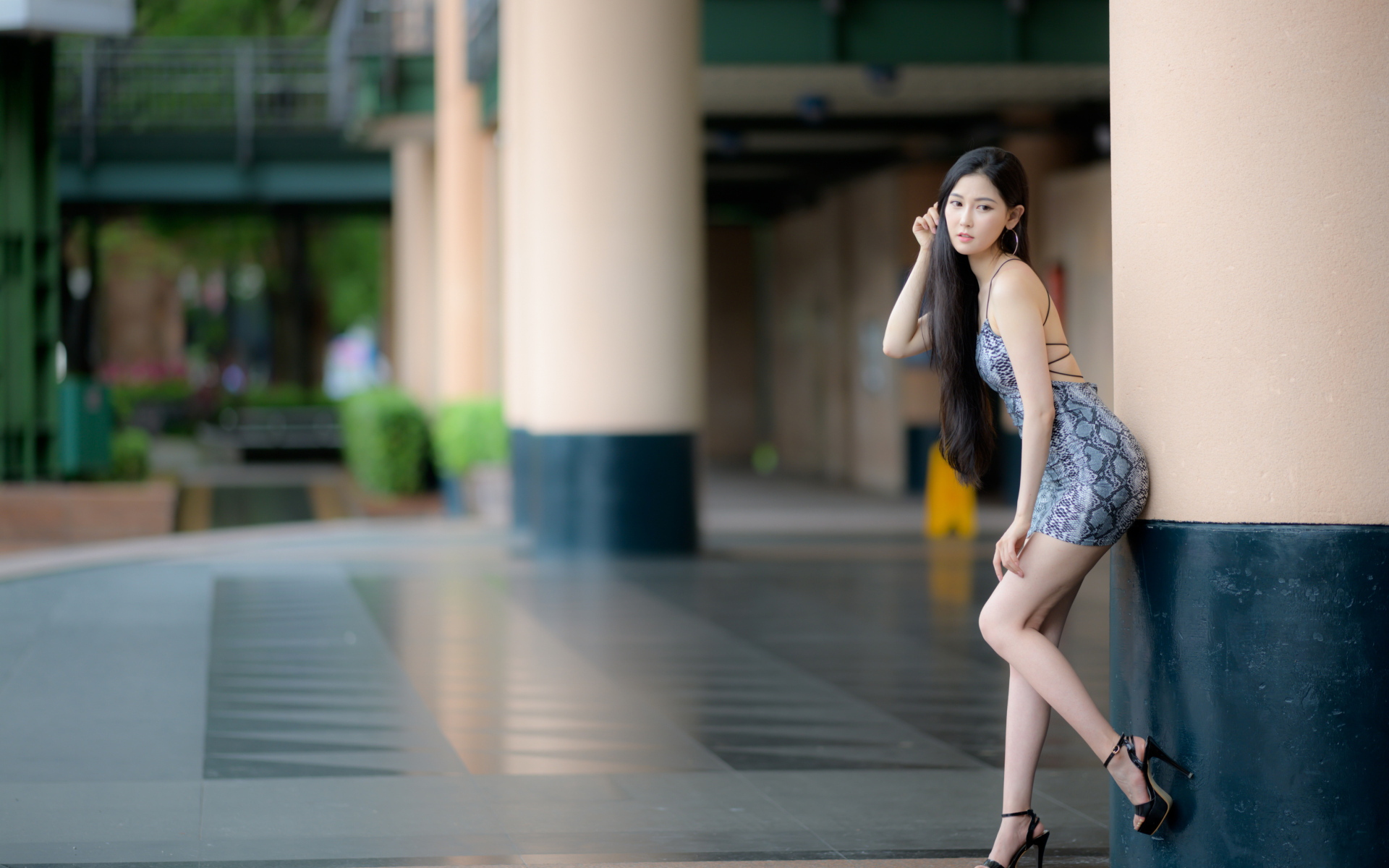 Стройная азиатка в коротком платье  стоит у колонны