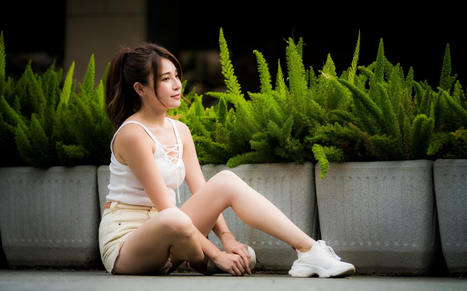 Девушка азиатка сидит на земле у зеленых растений