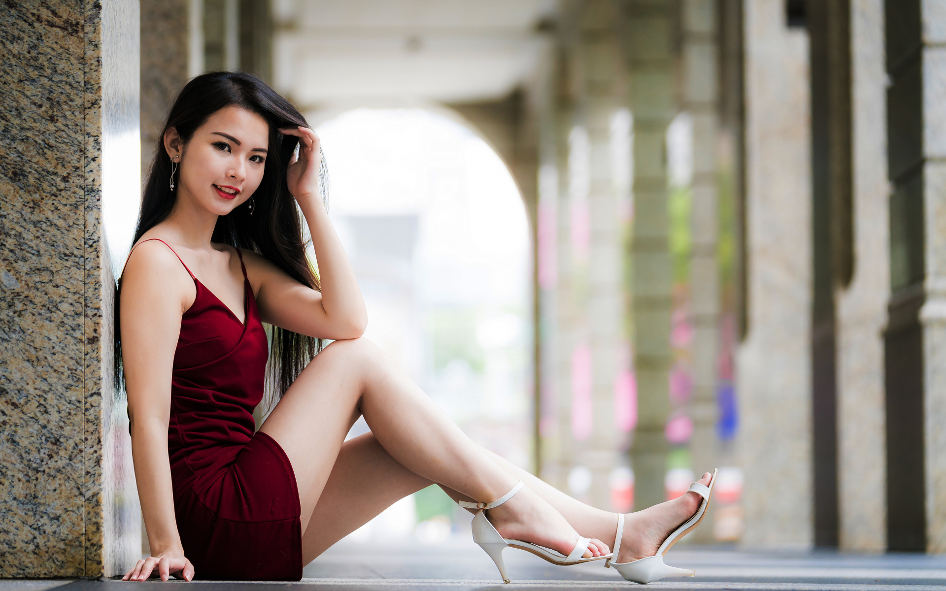 Азиатка в красном платье сидит у стены 