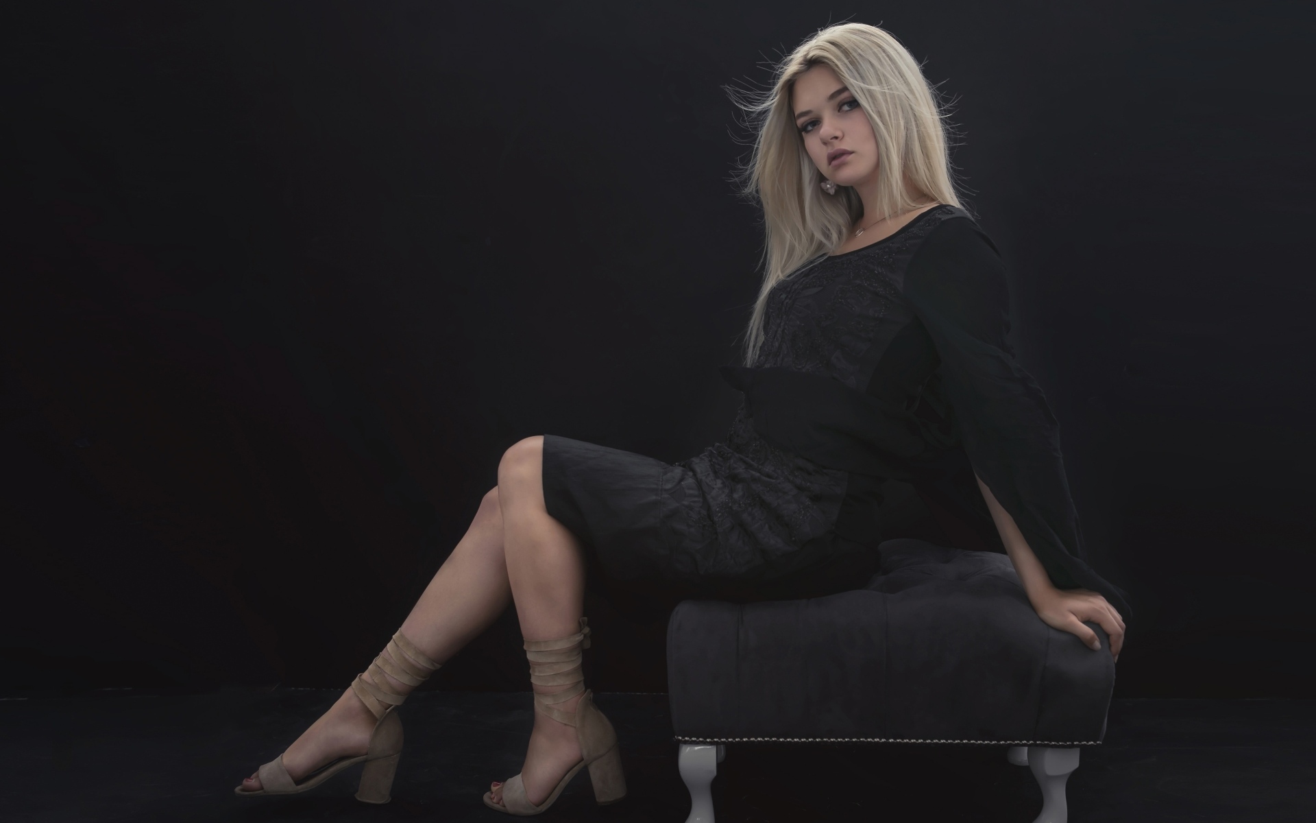 Красивая девушка в черном платье сидит на кресле