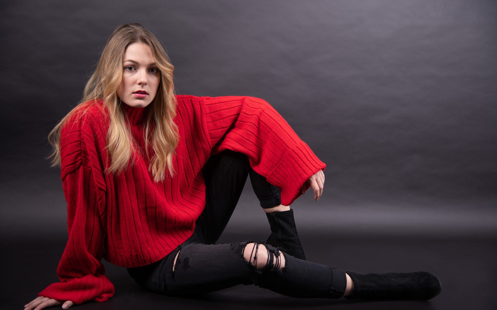 Девушка в красном свитере сидит на сером фоне