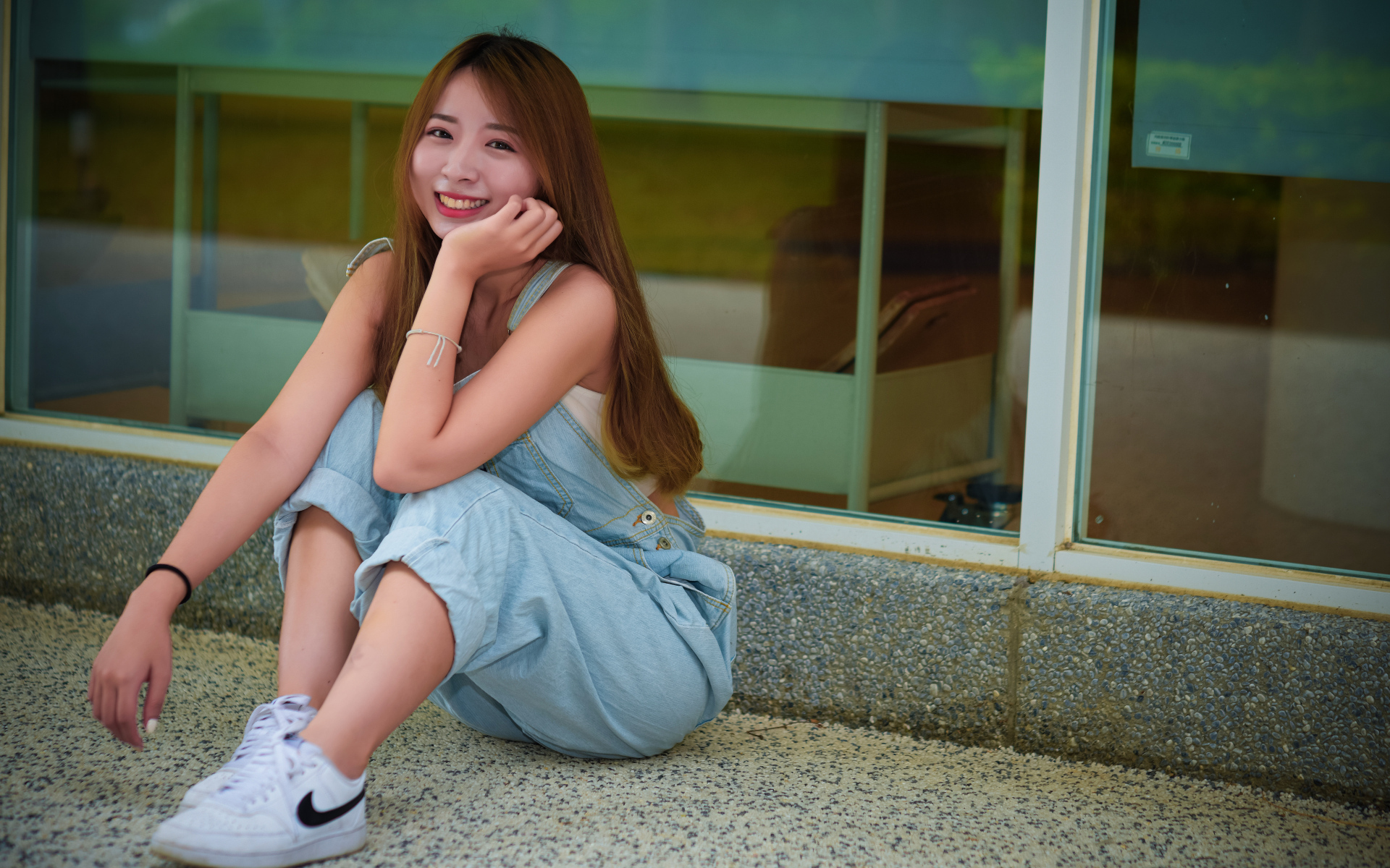 Девушка в джинсовом комбинезоне сидит на полу