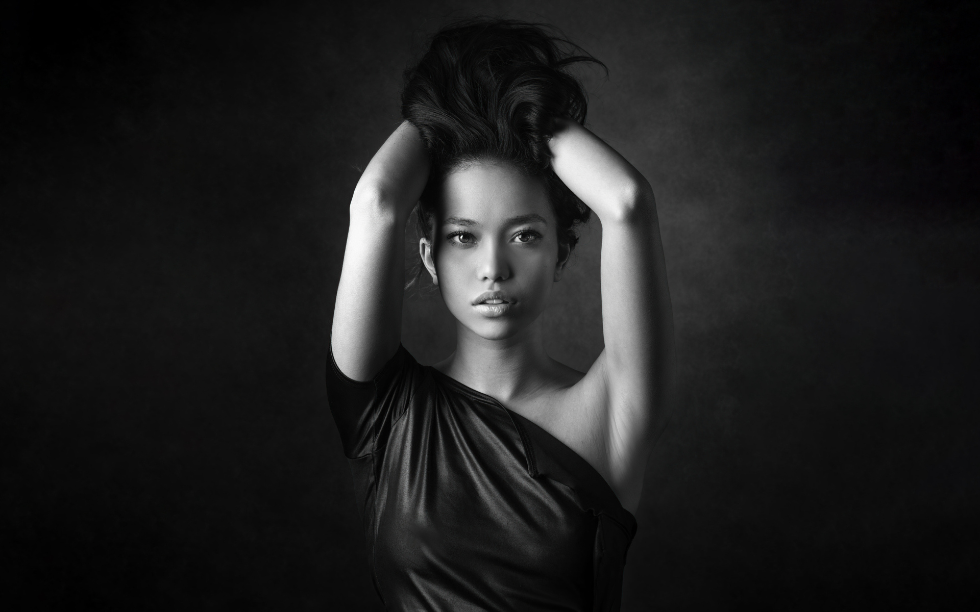 Девушка модель с руками в волосах  у стены