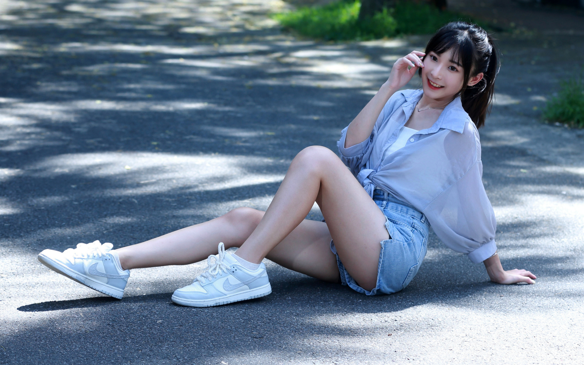 Улыбающаяся девушка азиатка в кедах сидит на дороге
