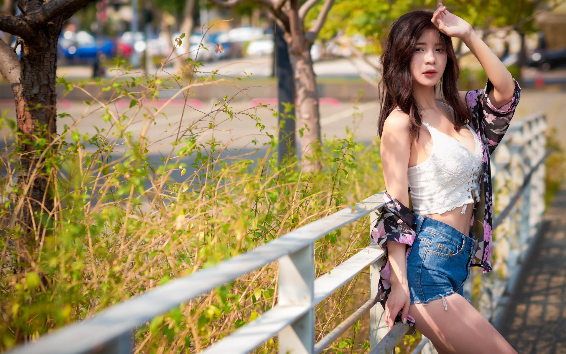 Молодая азиатка в синих шортах стоит у забора