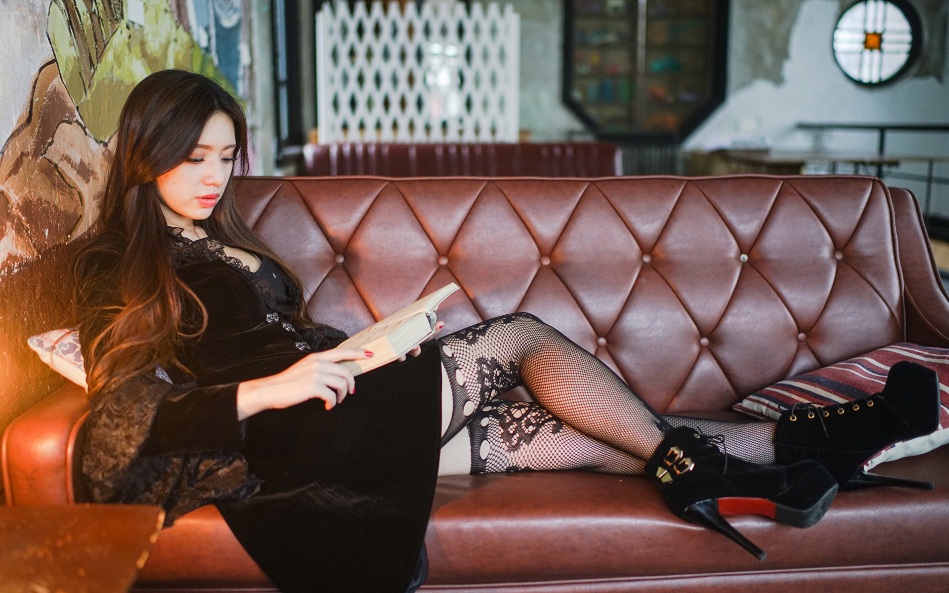 Молодая девушка читает книгу на кожаном диване