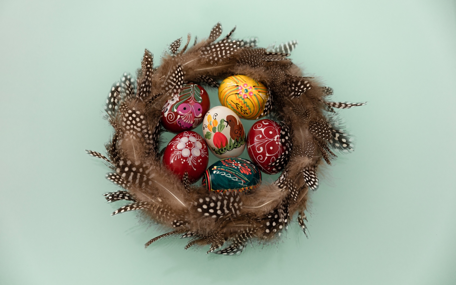 Красивые разноцветные яйца в гнезде из перьев на сером фоне