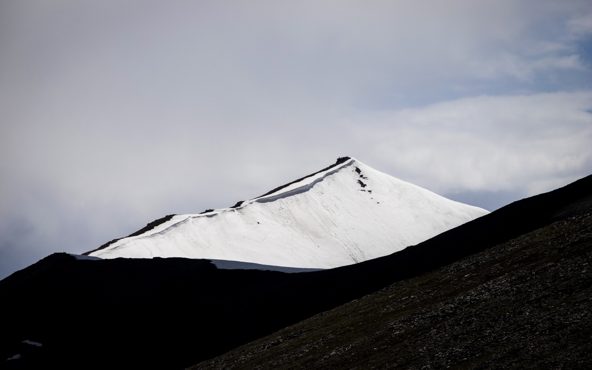 Заснеженная вершина горы под грозовым небом