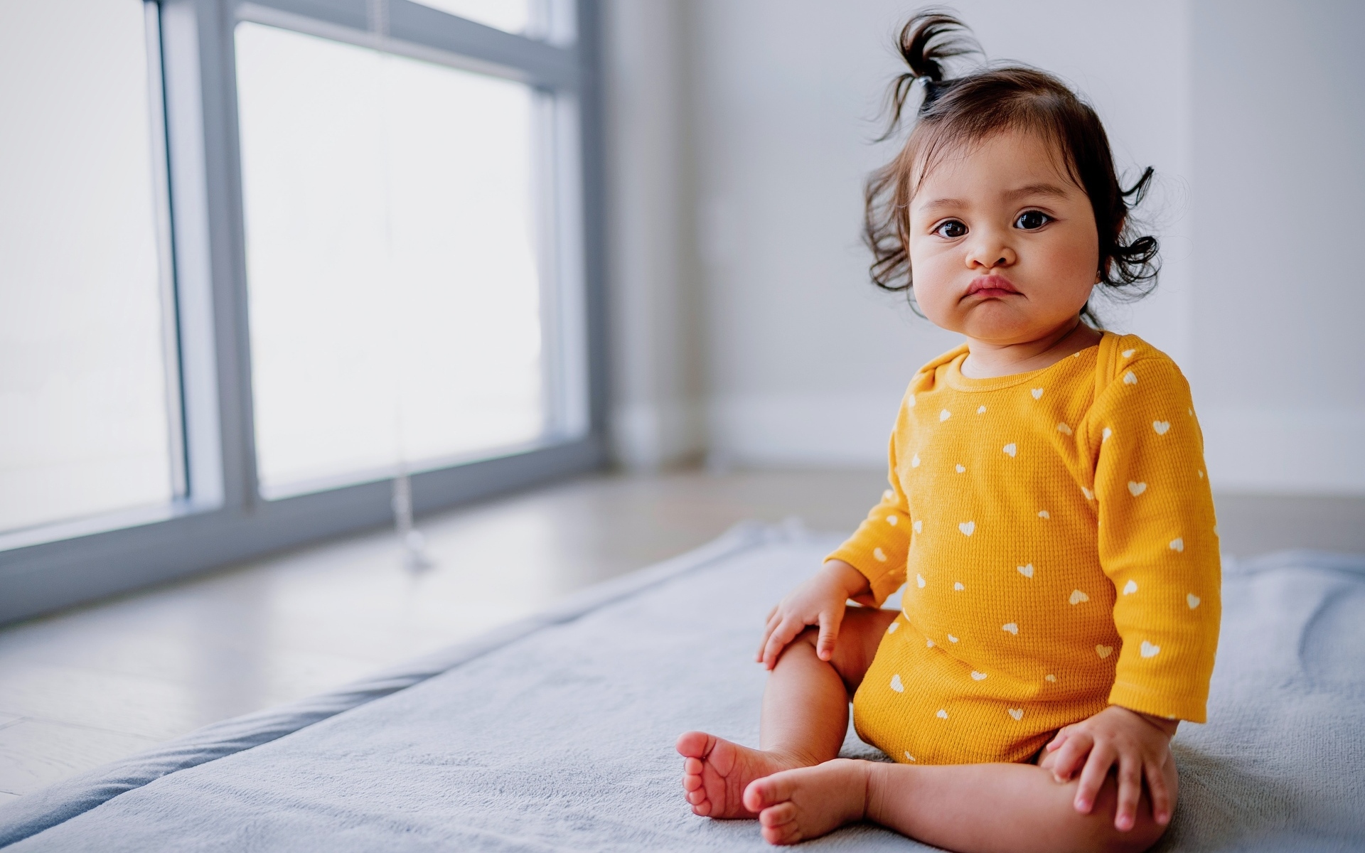 Маленькая смешная девочка сидит у окна