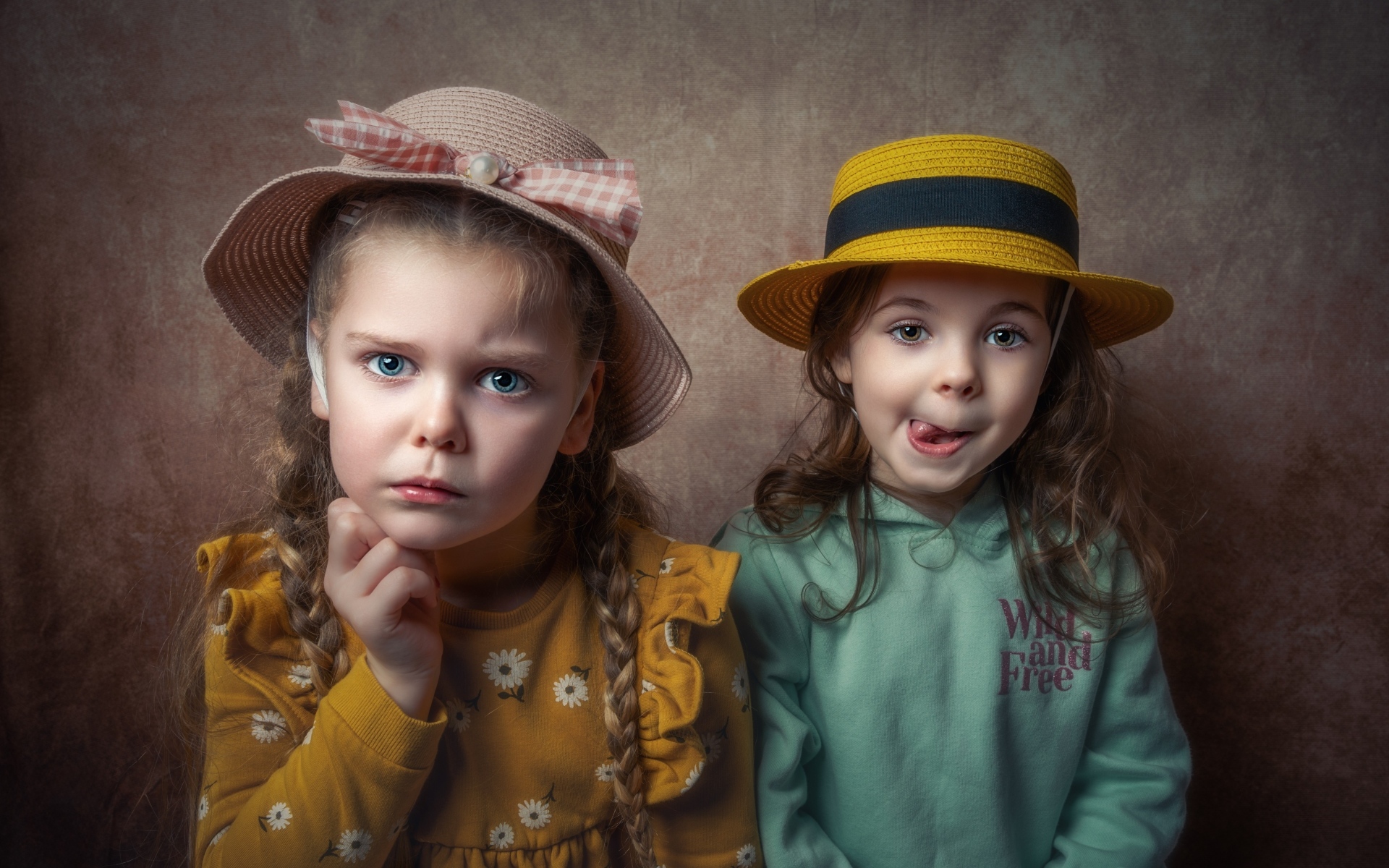Две маленькие девочки в шляпках на фоне коричневой стены