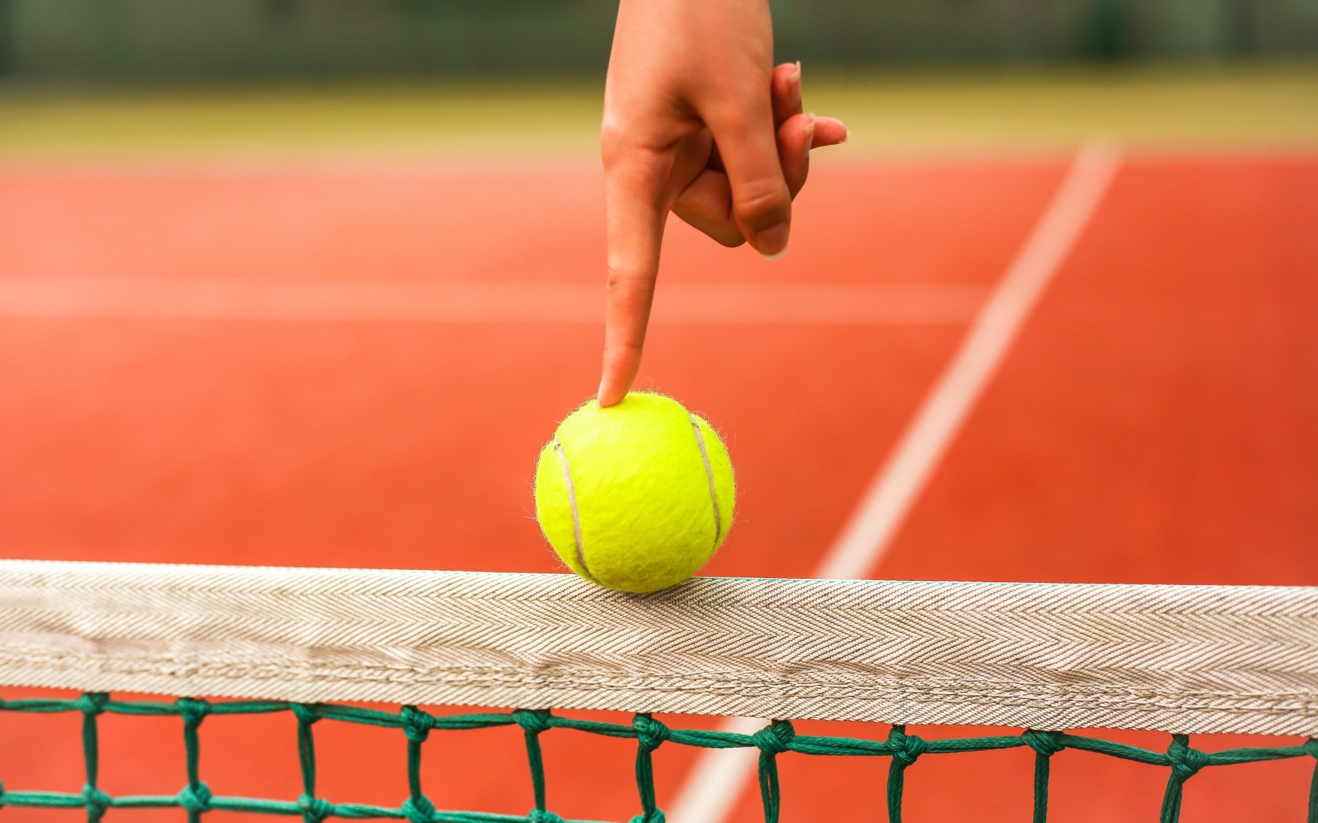 Палец держит желтый теннисный мяч