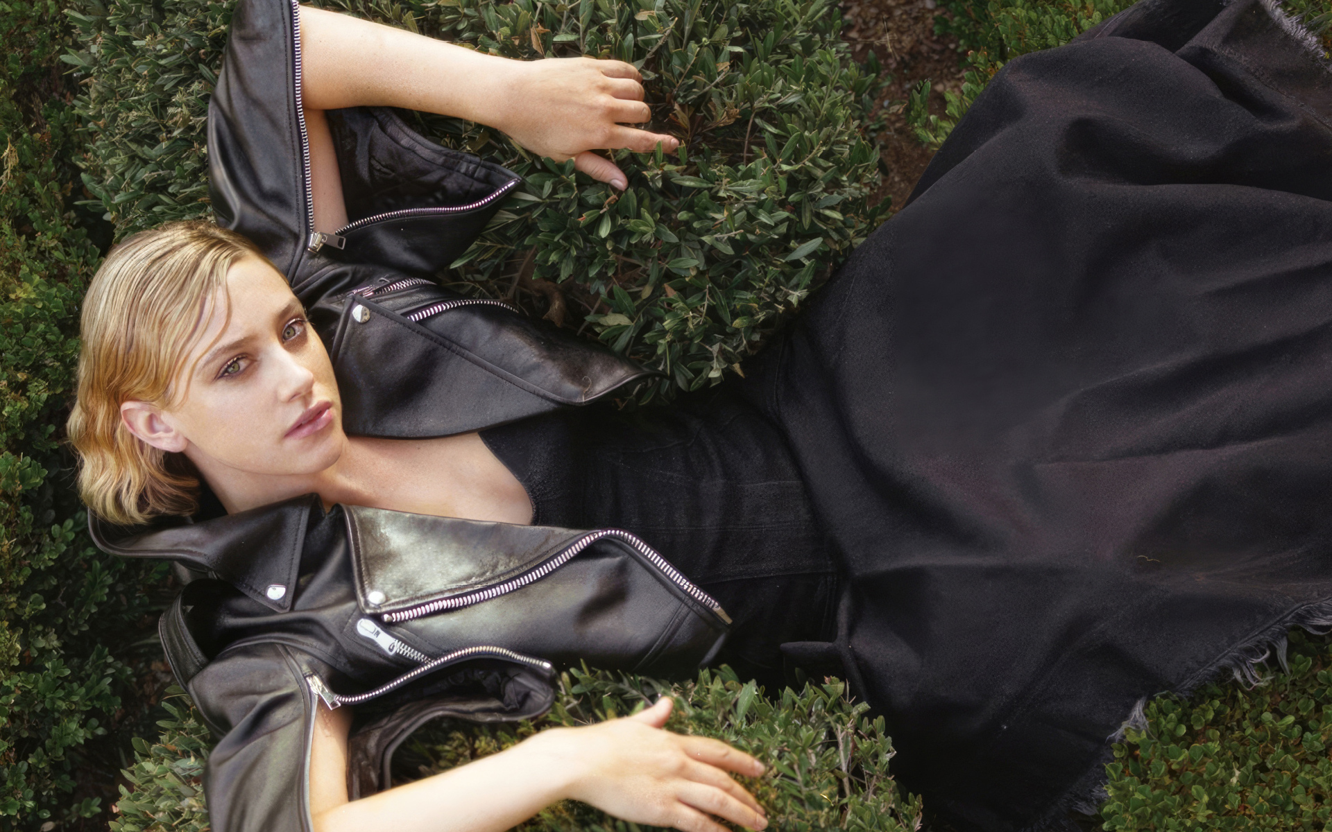 Актриса Лили Рейнхарт в черном костюме лежит в траве
