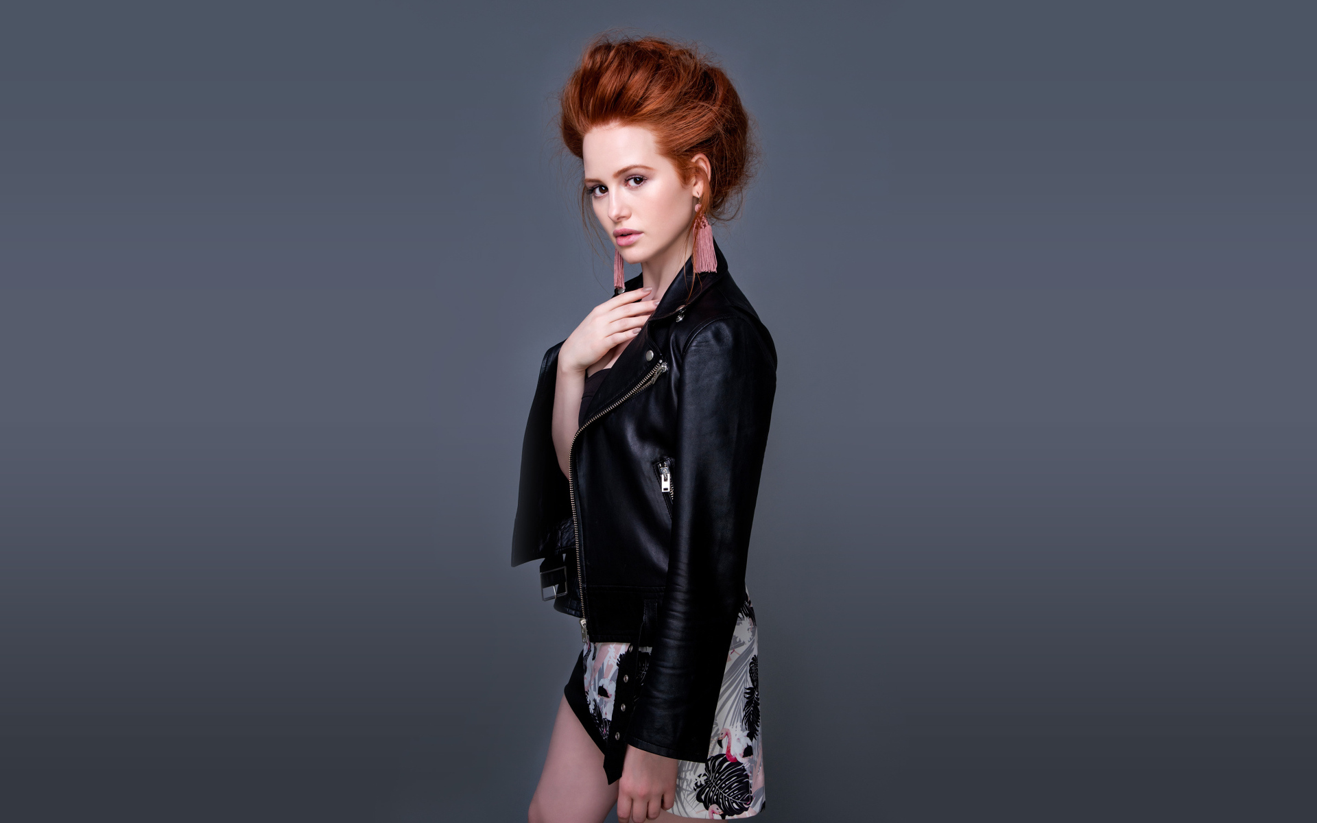 Рыжеволосая актриса Мэделин Петш в черной куртке на сером фоне