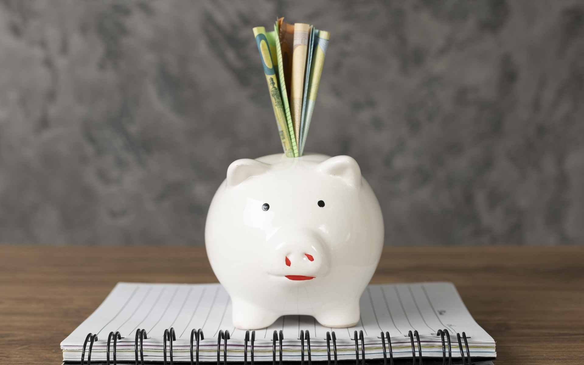 Свинья копилка с купюрами на столе с блокнотом