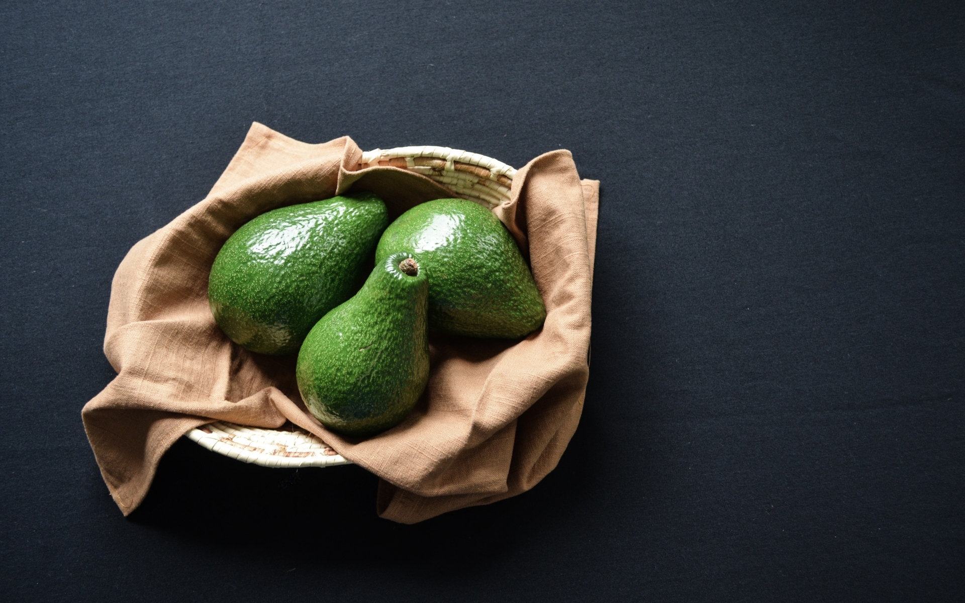 Три зеленых авокадо в корзинке на столе