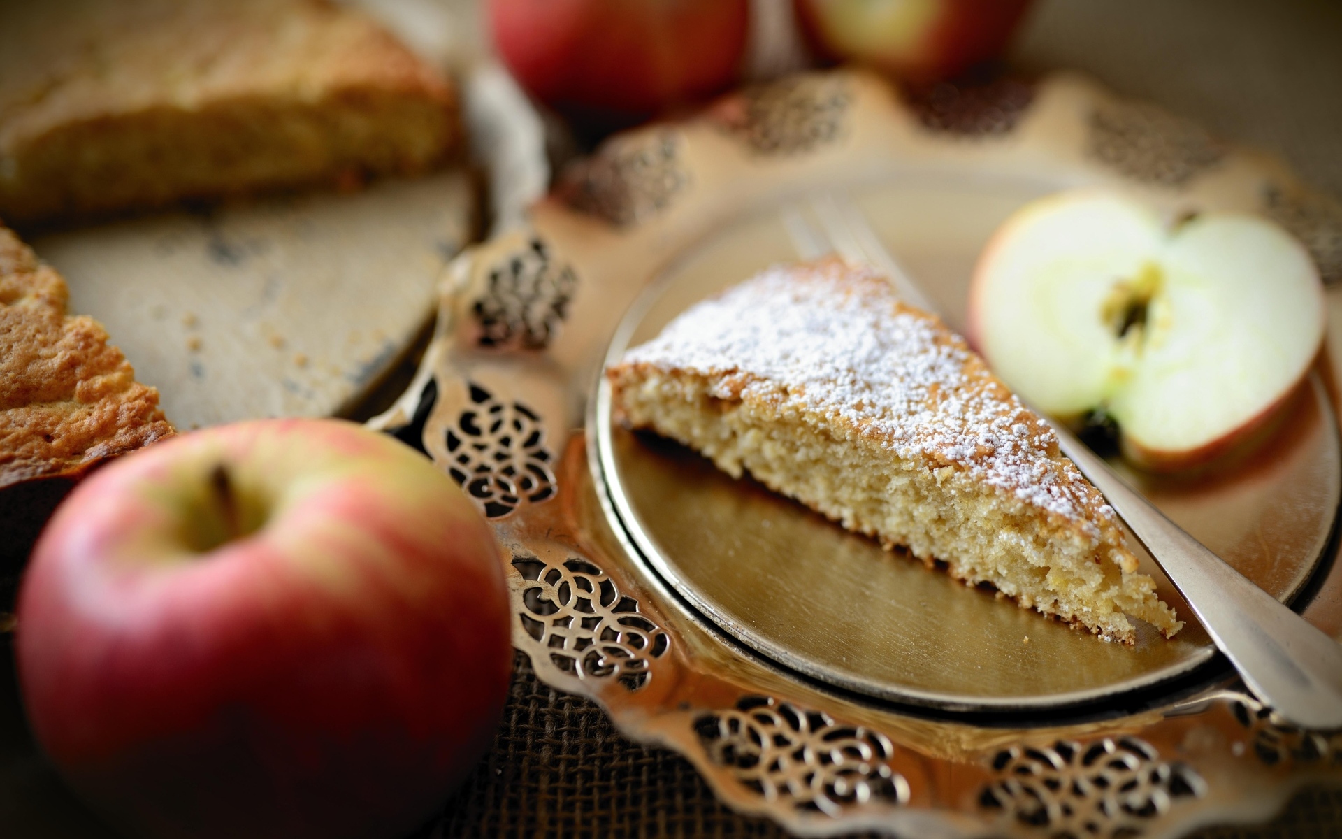 Кусок пирога с сахарной пудрой на столе с яблоками
