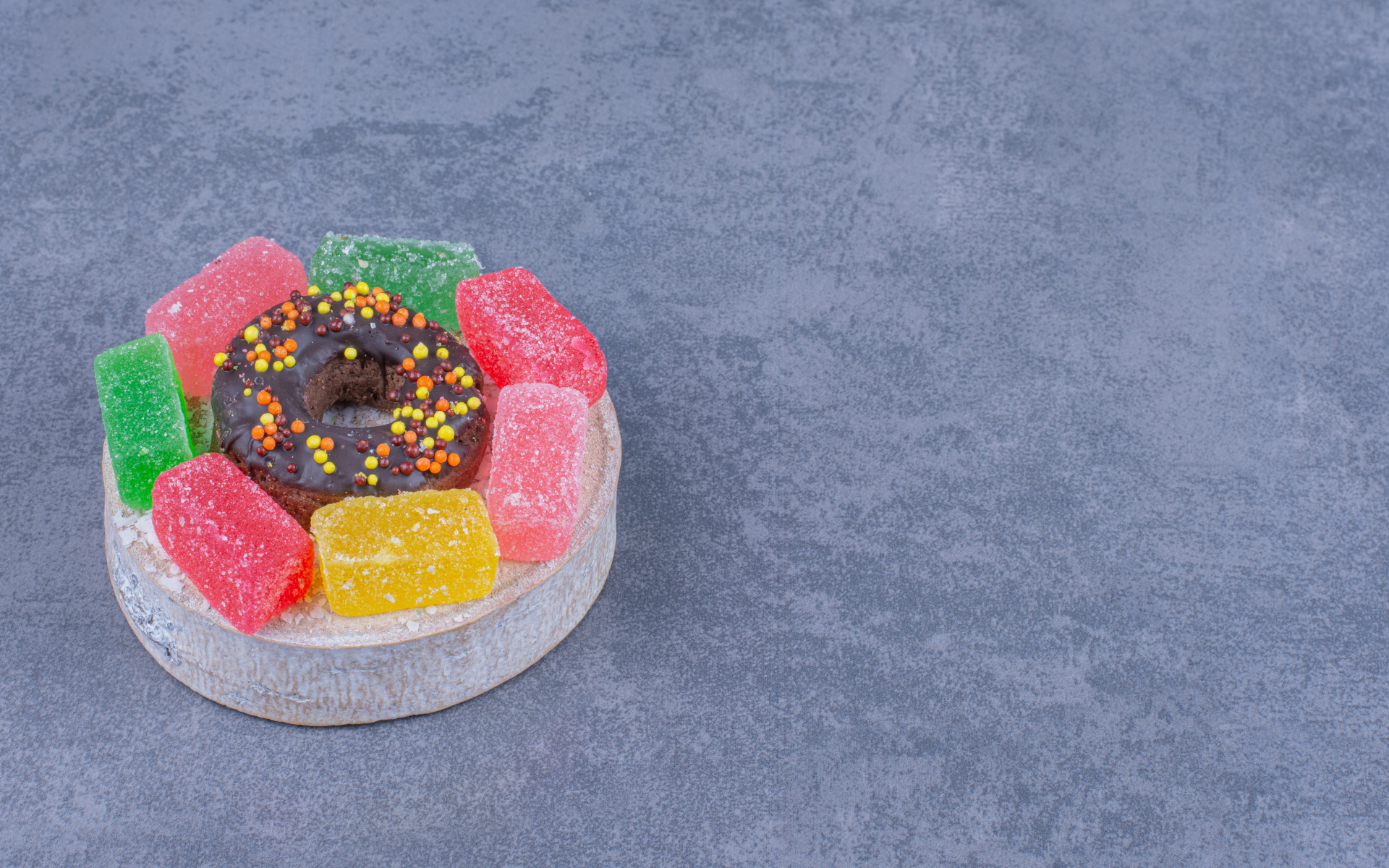 Разноцветные мармеладные конфеты и пончик на сером столе