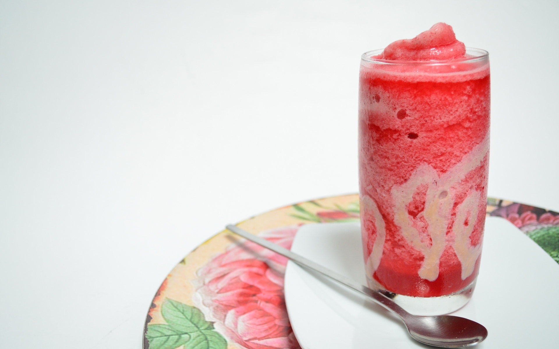 Стакан красного ягодного смузи на столе с чайной ложкой