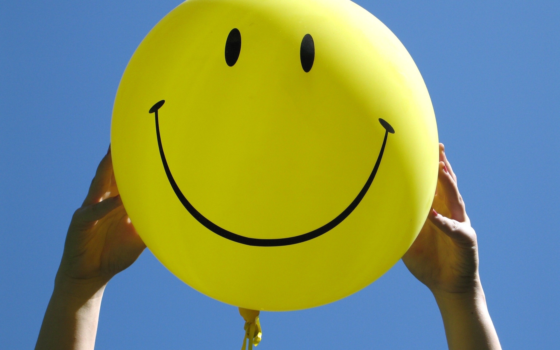 Желтый шарик с улыбкой в руках на голубом фоне