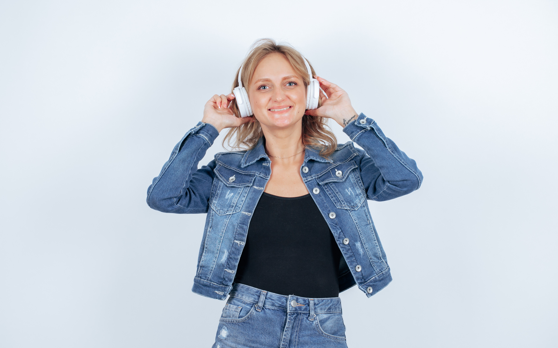 Девушка в джинсовом костюме с наушниками на голове на фоне стены