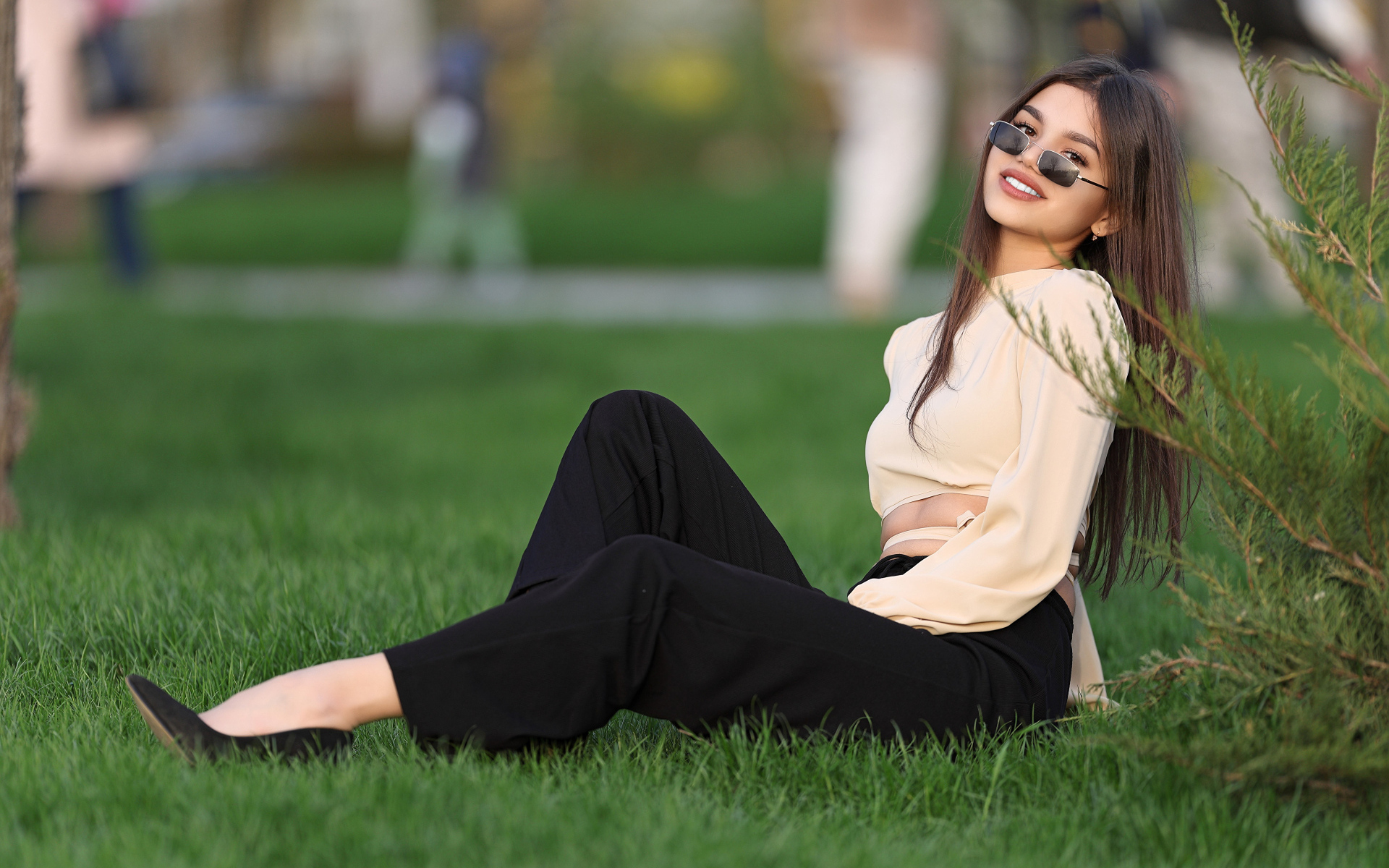 Девушка в черных брюках и блузке сидит на траве