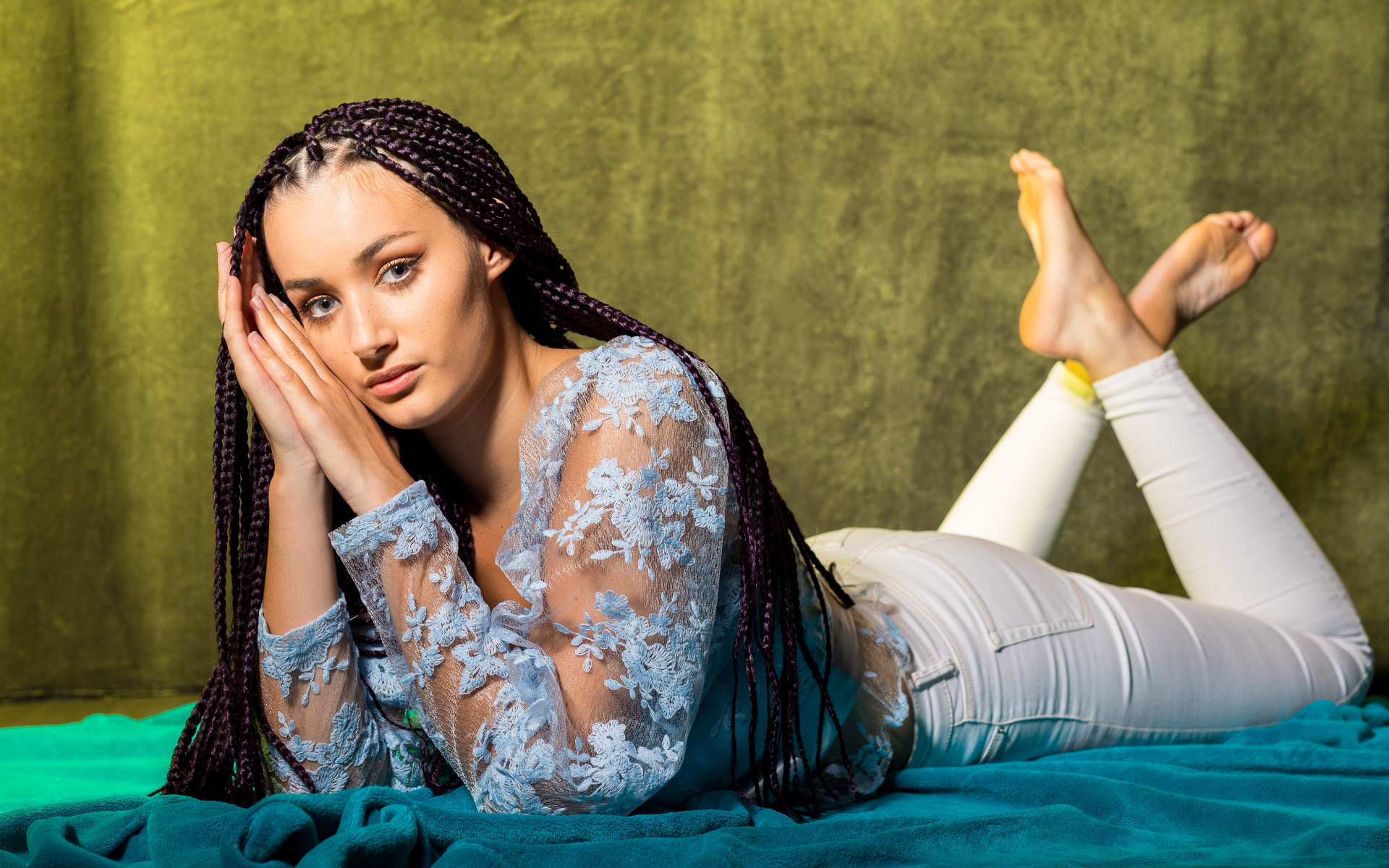 Брюнетка с косами на голове лежит на постели