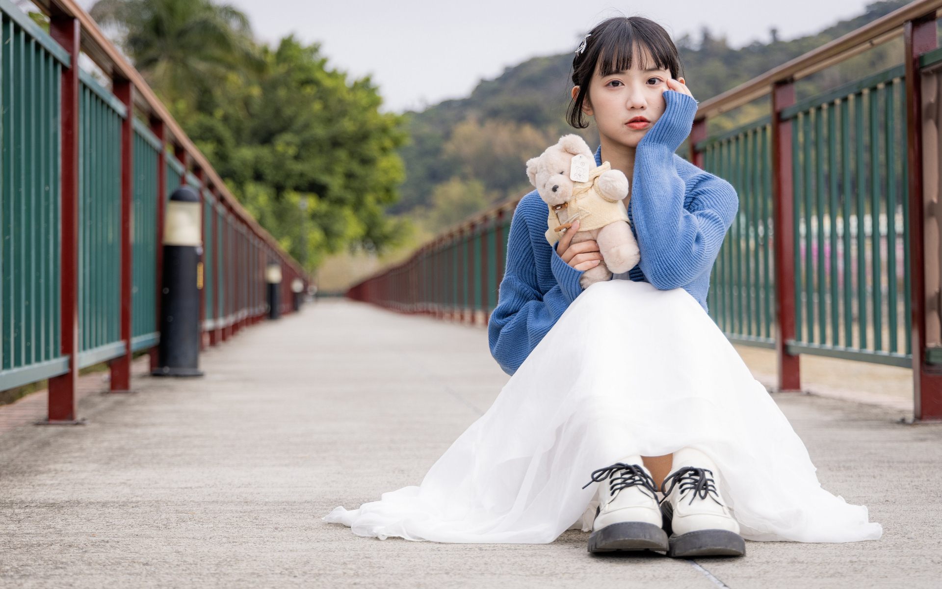 Милая азиатка с игрушечным медвежонком сидит на мосту