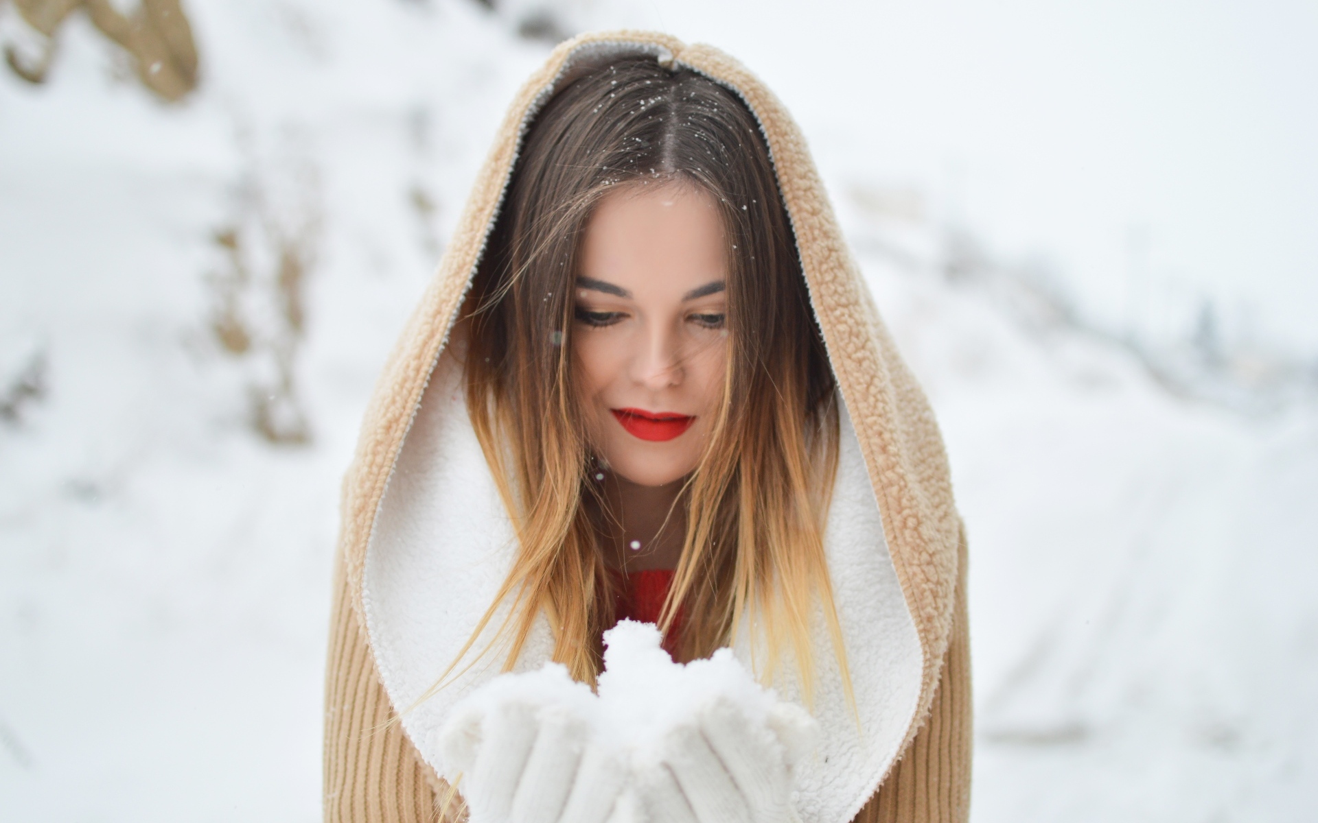 Милая девушка в капюшоне держит снег в ладонях