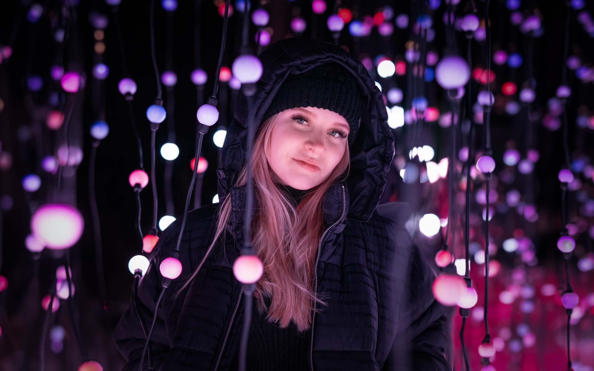 Девушка в черной куртке у светящейся гирлянды
