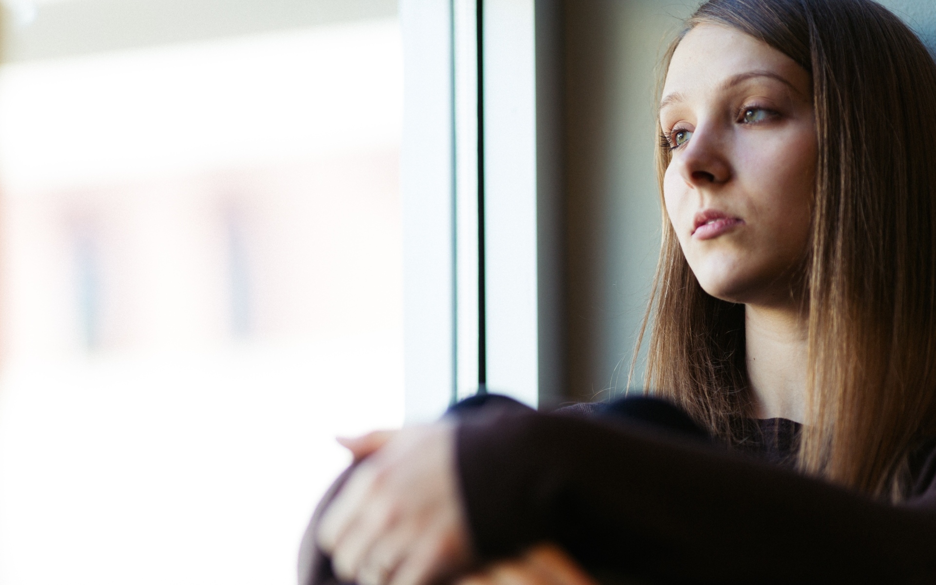 Грустная девушка сидит у окна