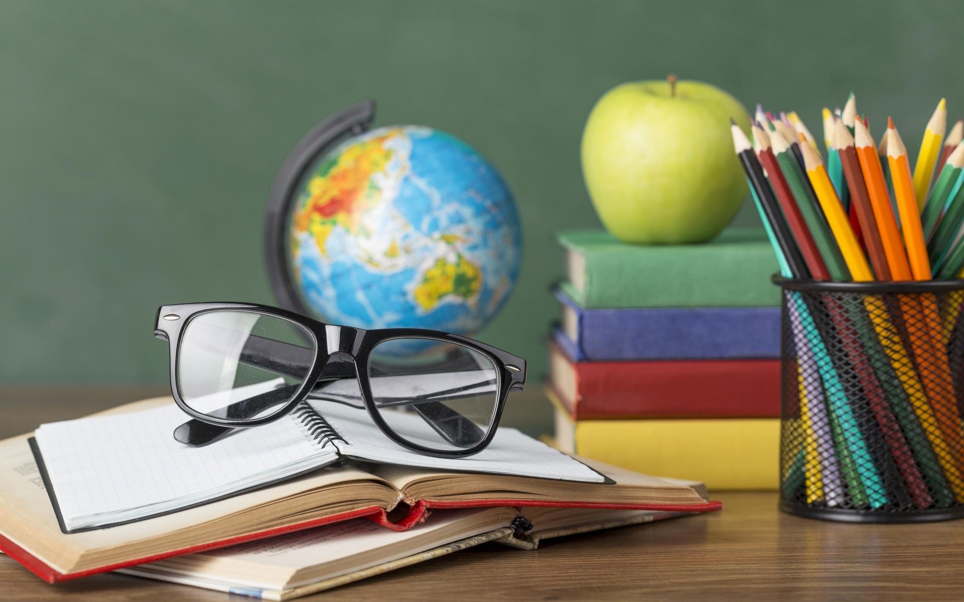 Книги, очки и карандаши с глобусом на столе у доски