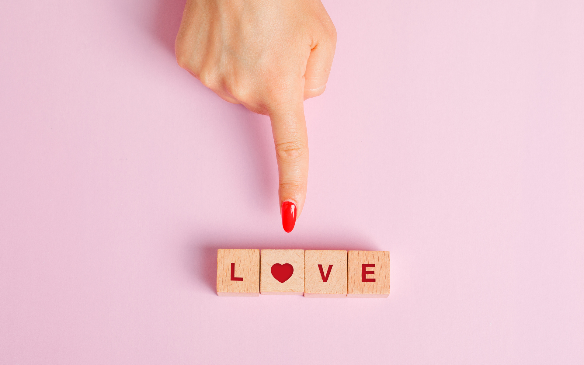 Рука указывает на кубики с надписью любовь на розовом фоне