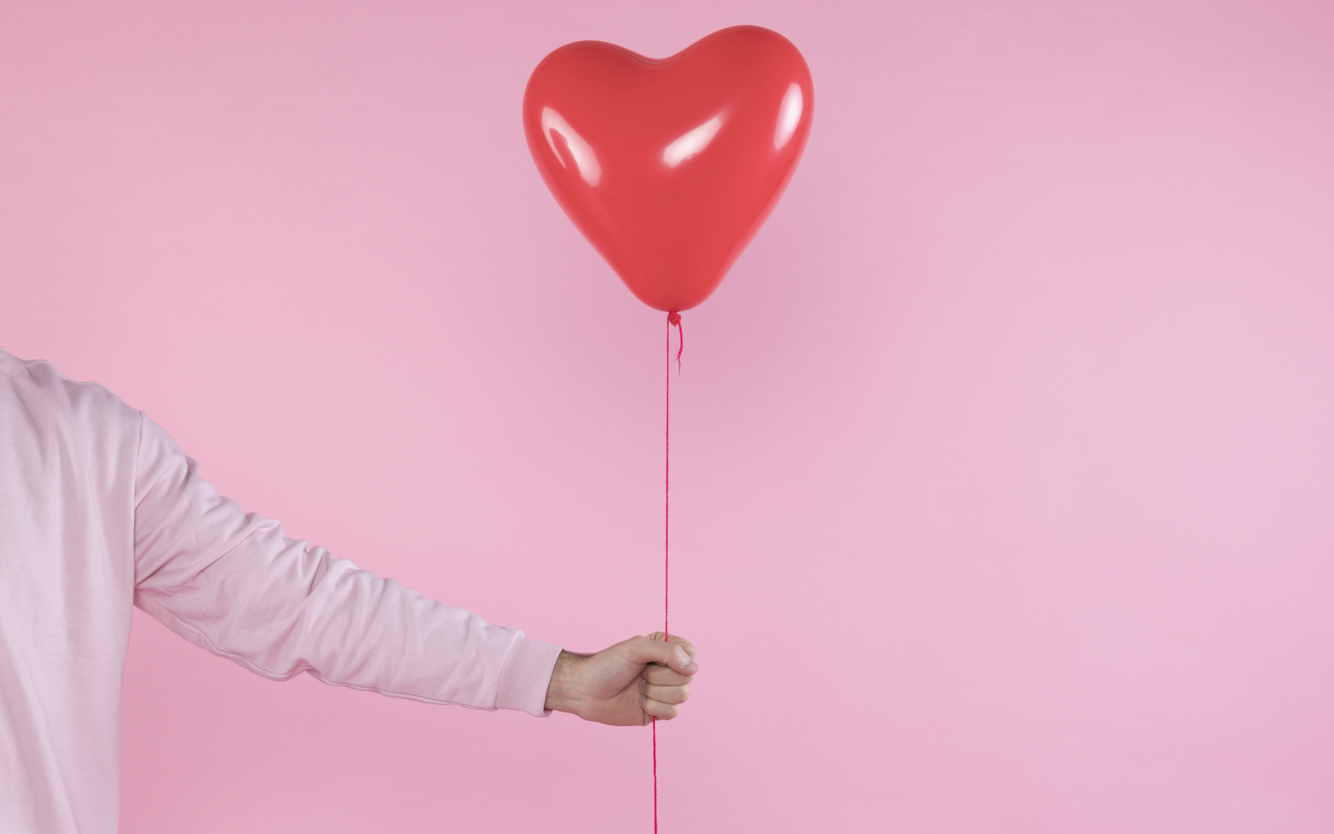 Шарик в форме сердца в руке на розовом фоне