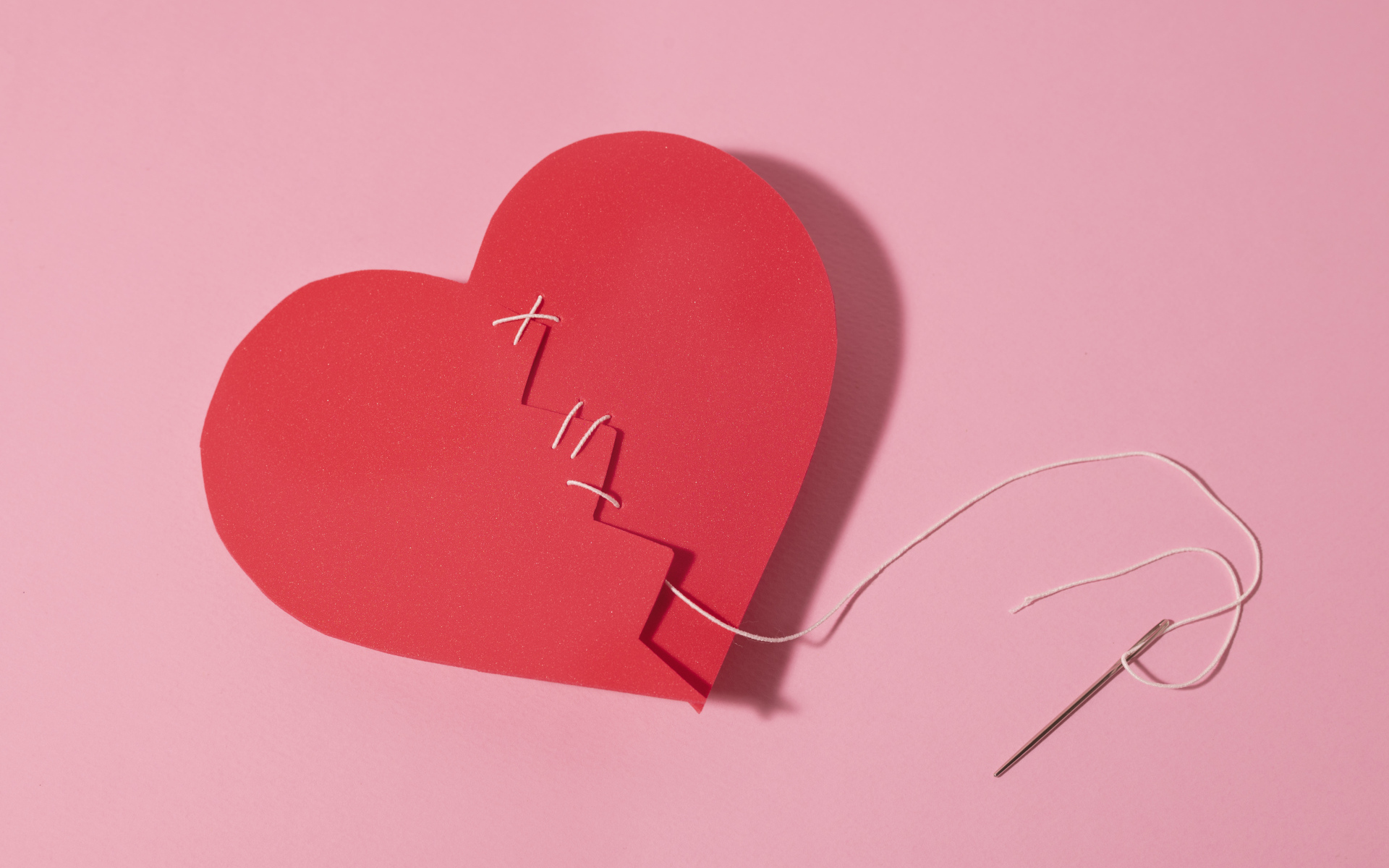 Бумажное сердце сшили нитками на розовом фоне
