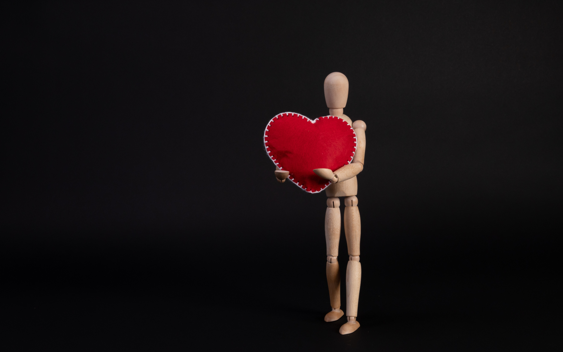 Марионетка держит красное сердце на черном фоне