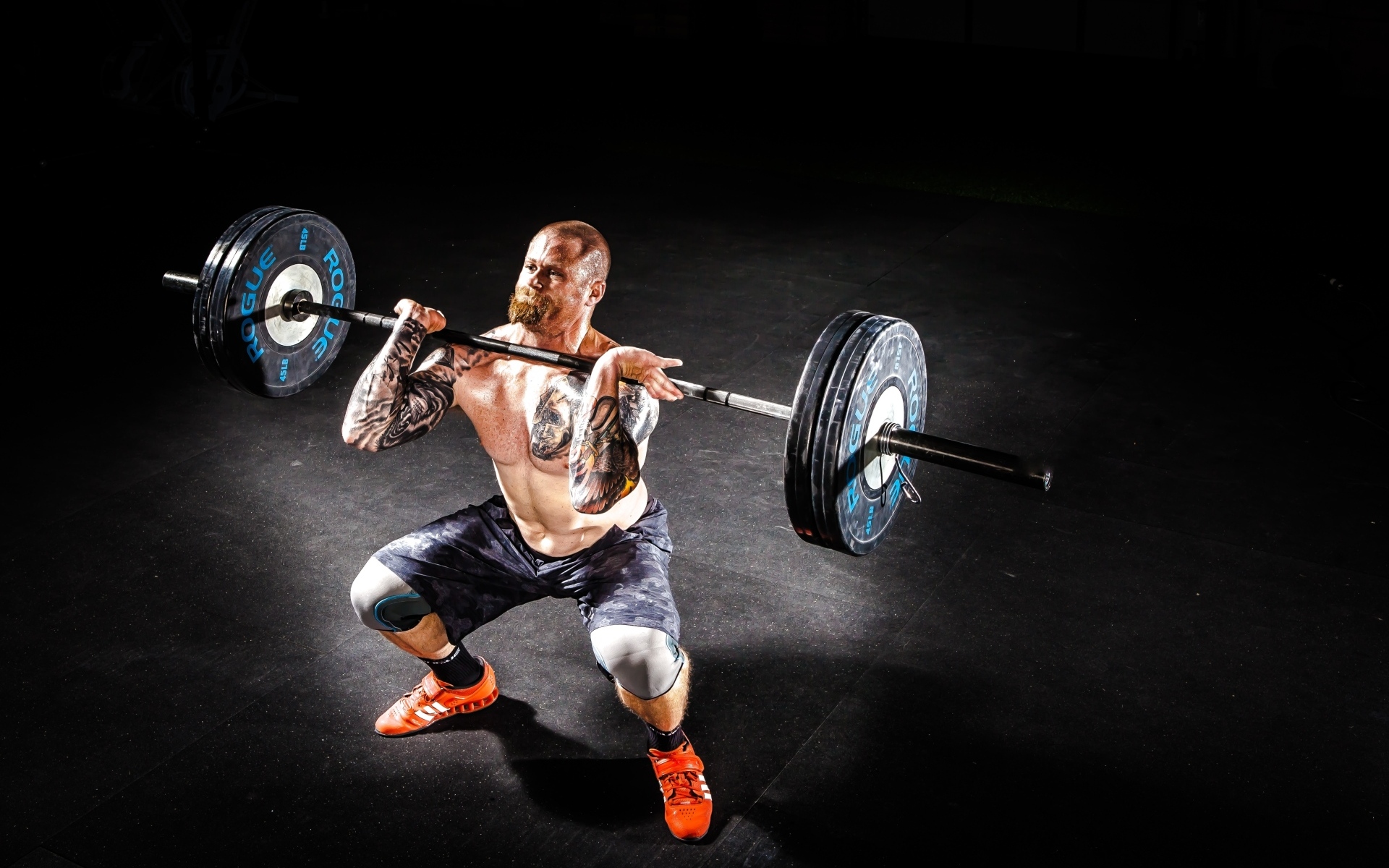 Сильный мужчина с татуировками на теле поднимает штангу