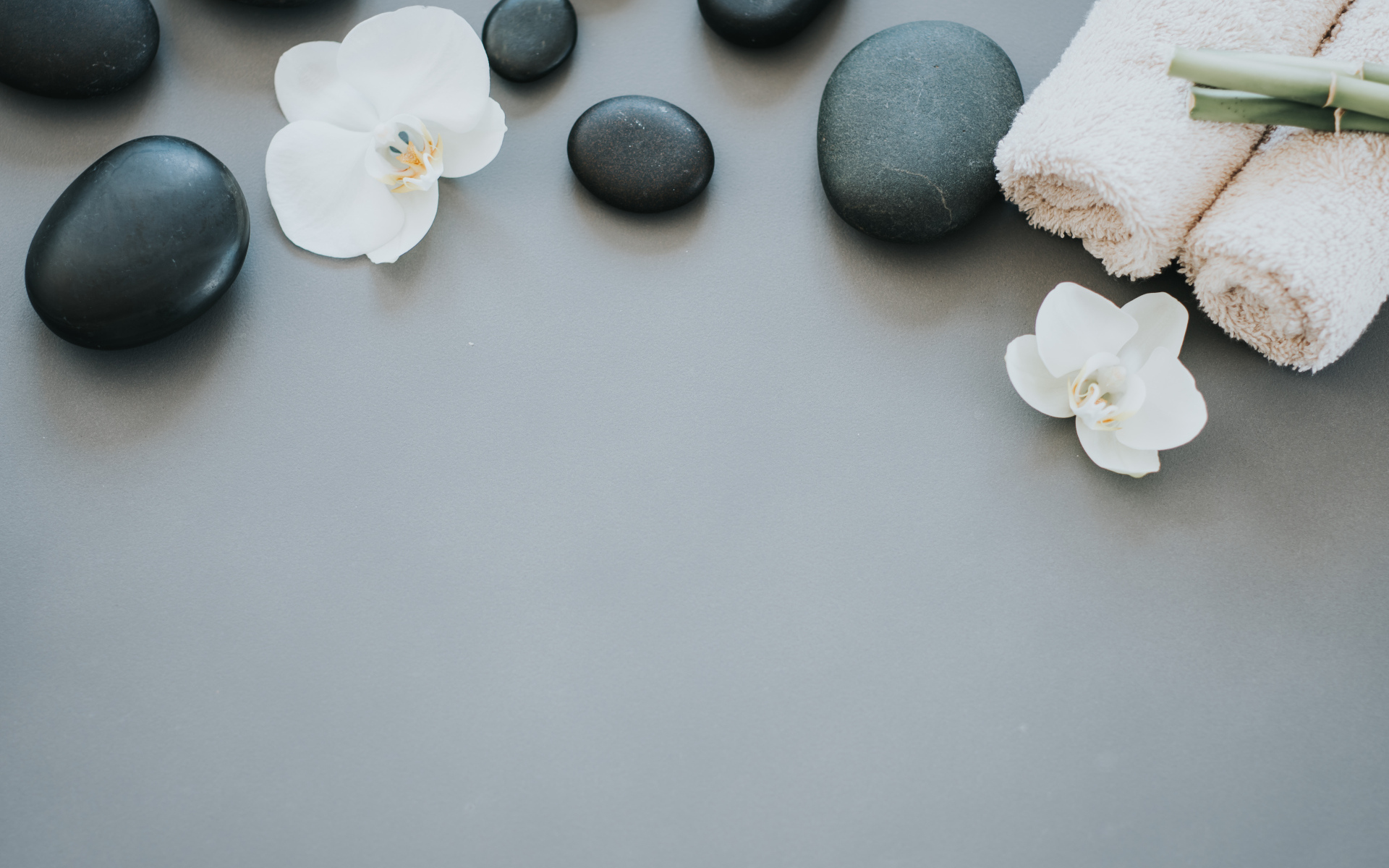 Черные камни с цветами орхидеи и полотенцем на сером фоне