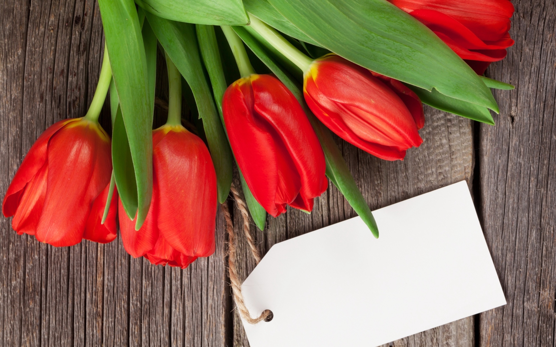 Букет красных тюльпанов с открыткой на деревянном столе
